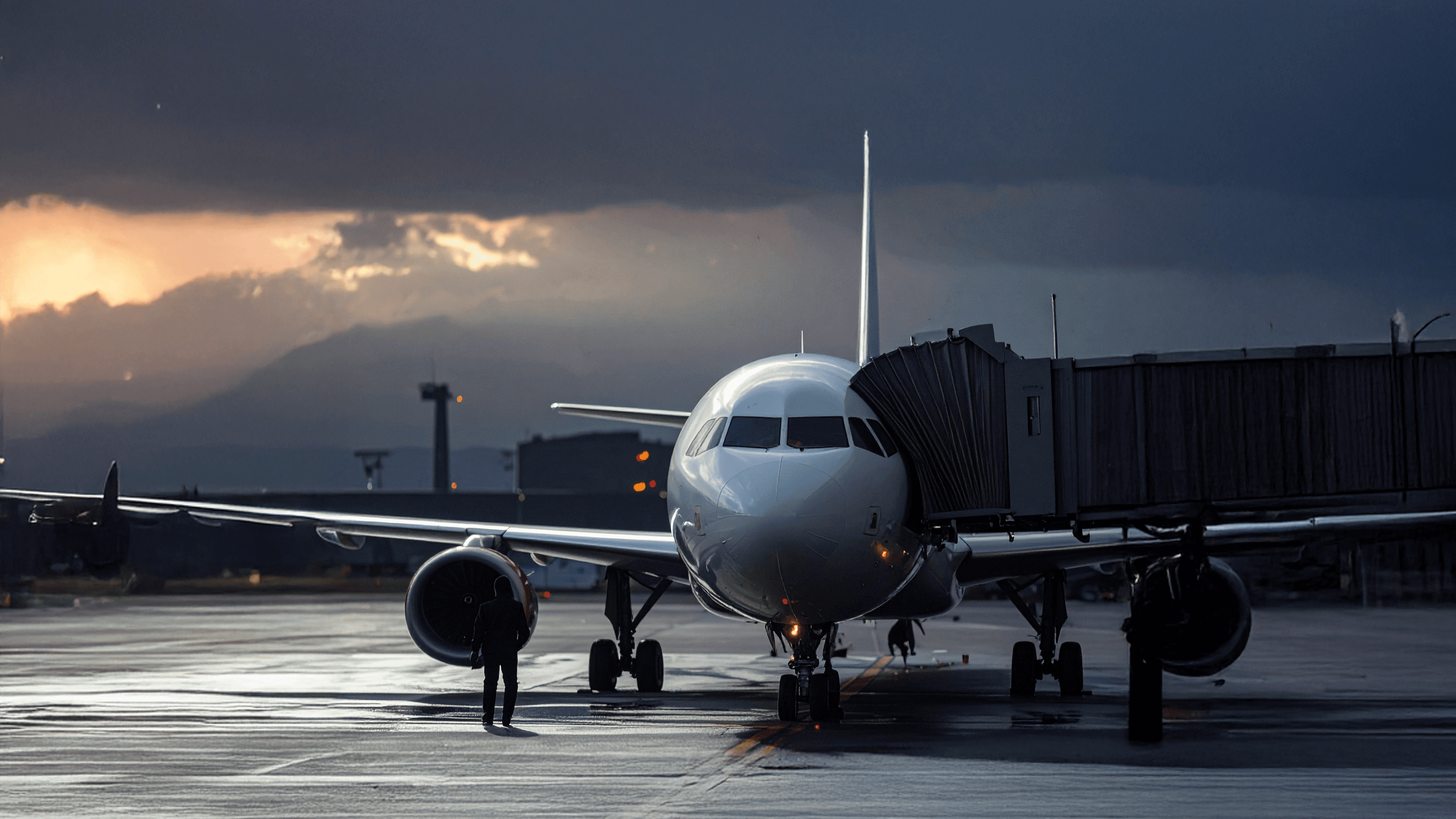 Flugzeug am Gate mit angedocktem Fluggastbrücke. Dramatischer Himmel und Berge im Hintergrund.