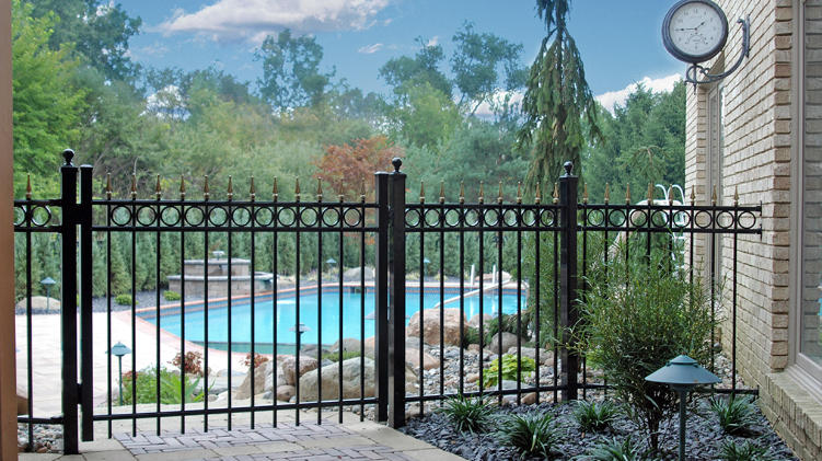 A black traditional aluminum walk gate and fence with exposed spear tops installed in front of a backyard pool.
