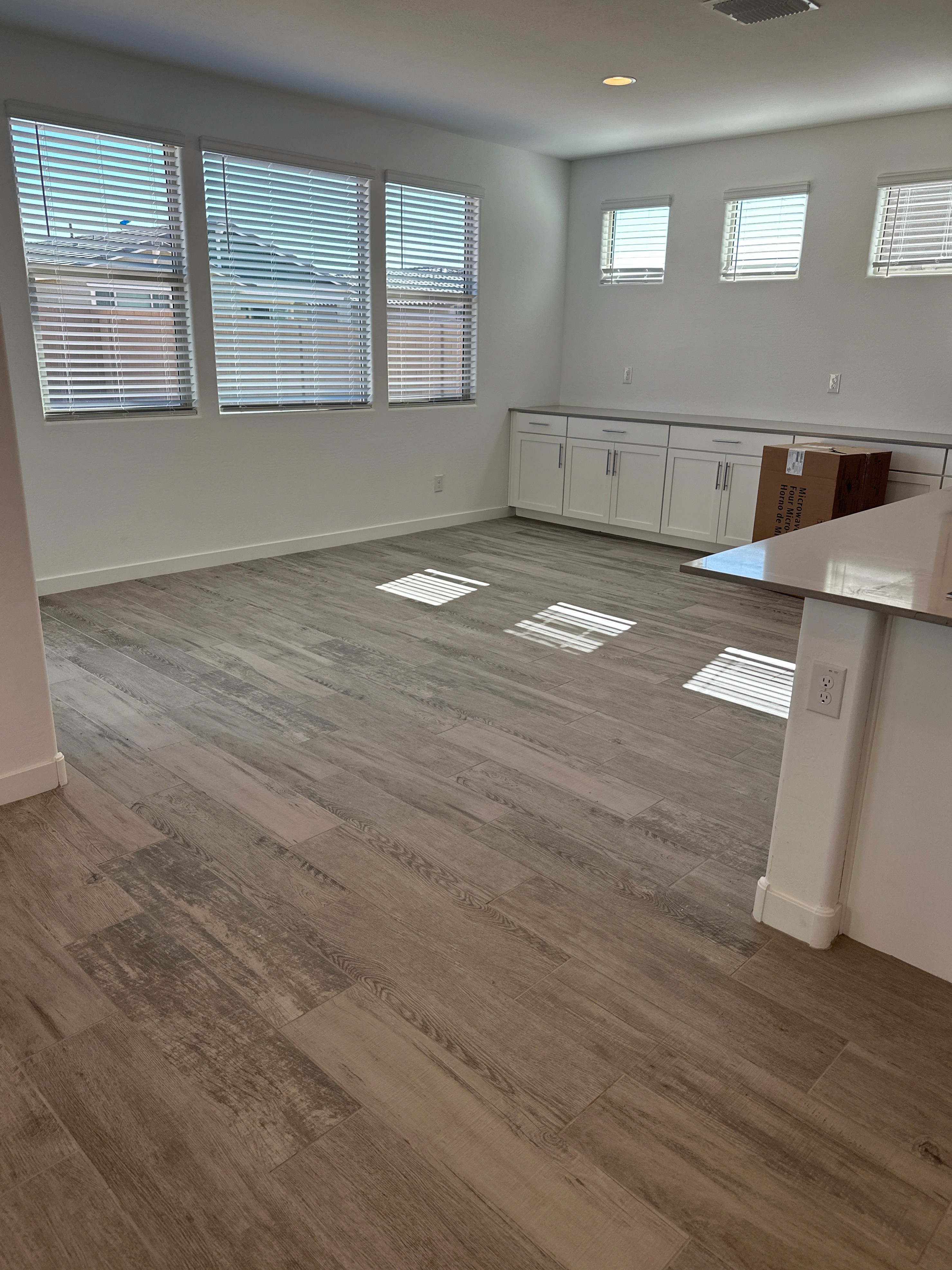 Modern kitchen with white cabinets, wood-look flooring, large windows, and natural light illuminating the open space during construction.