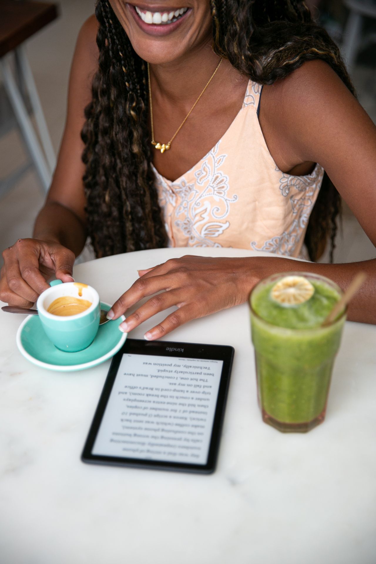 cafe table with a coffee, green drink and kindle on the table