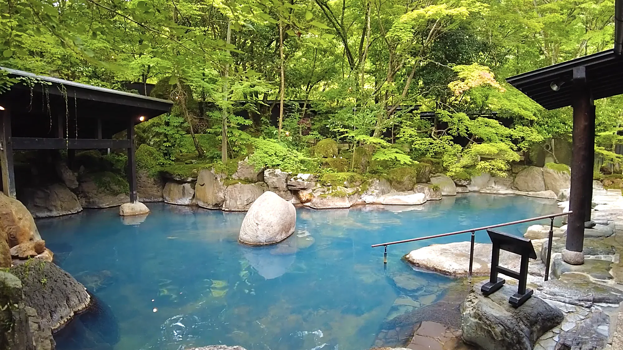 A milky blue garden pool among boulders and moss