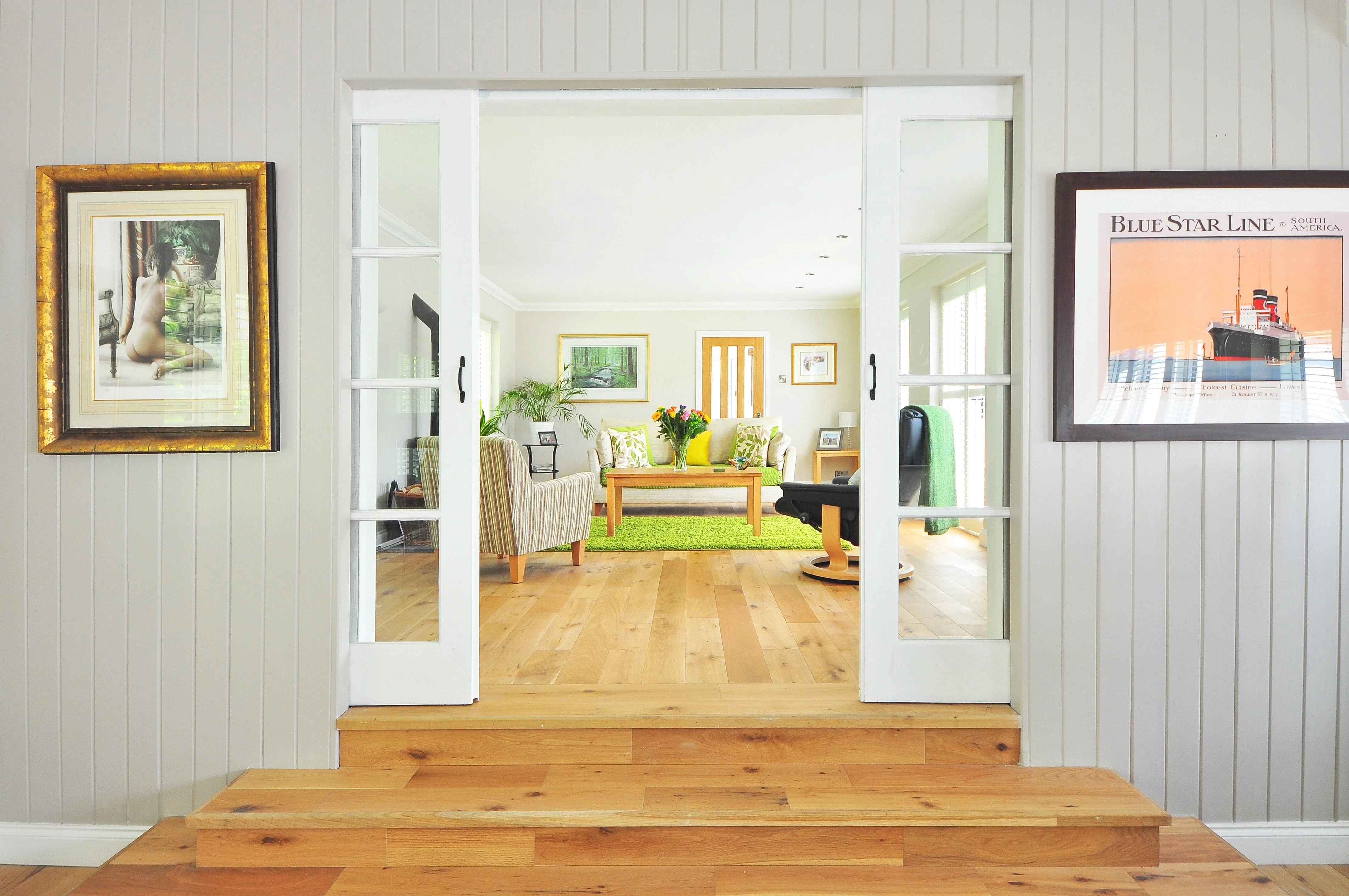 iew through white double doors into a brightly lit living room with framed wall art.