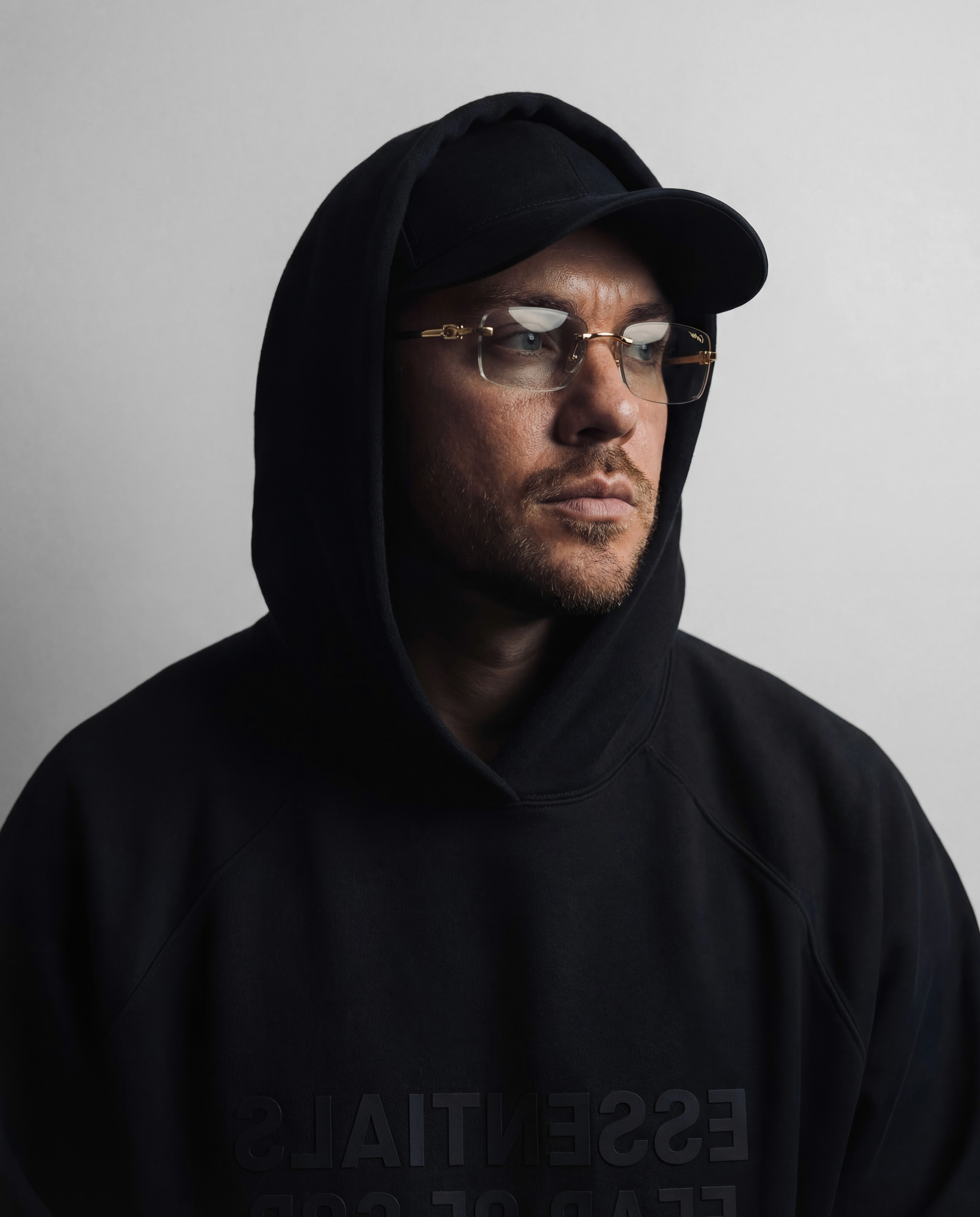 Close-up portrait of a person wearing a gray insulated hooded jacket with the hood up, showing their face framed by the hood against a light background.