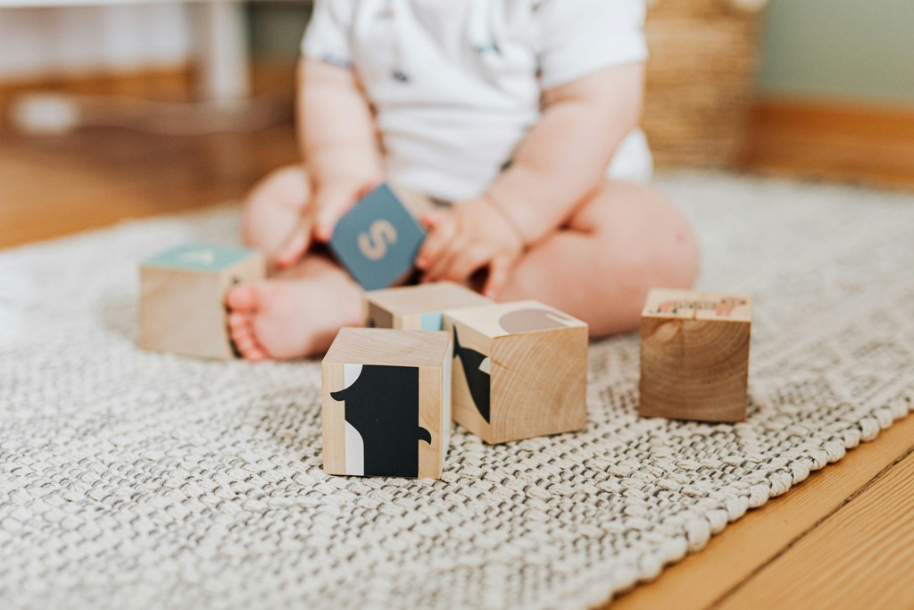 Obscured view of an infant playing with blocks on a rug.