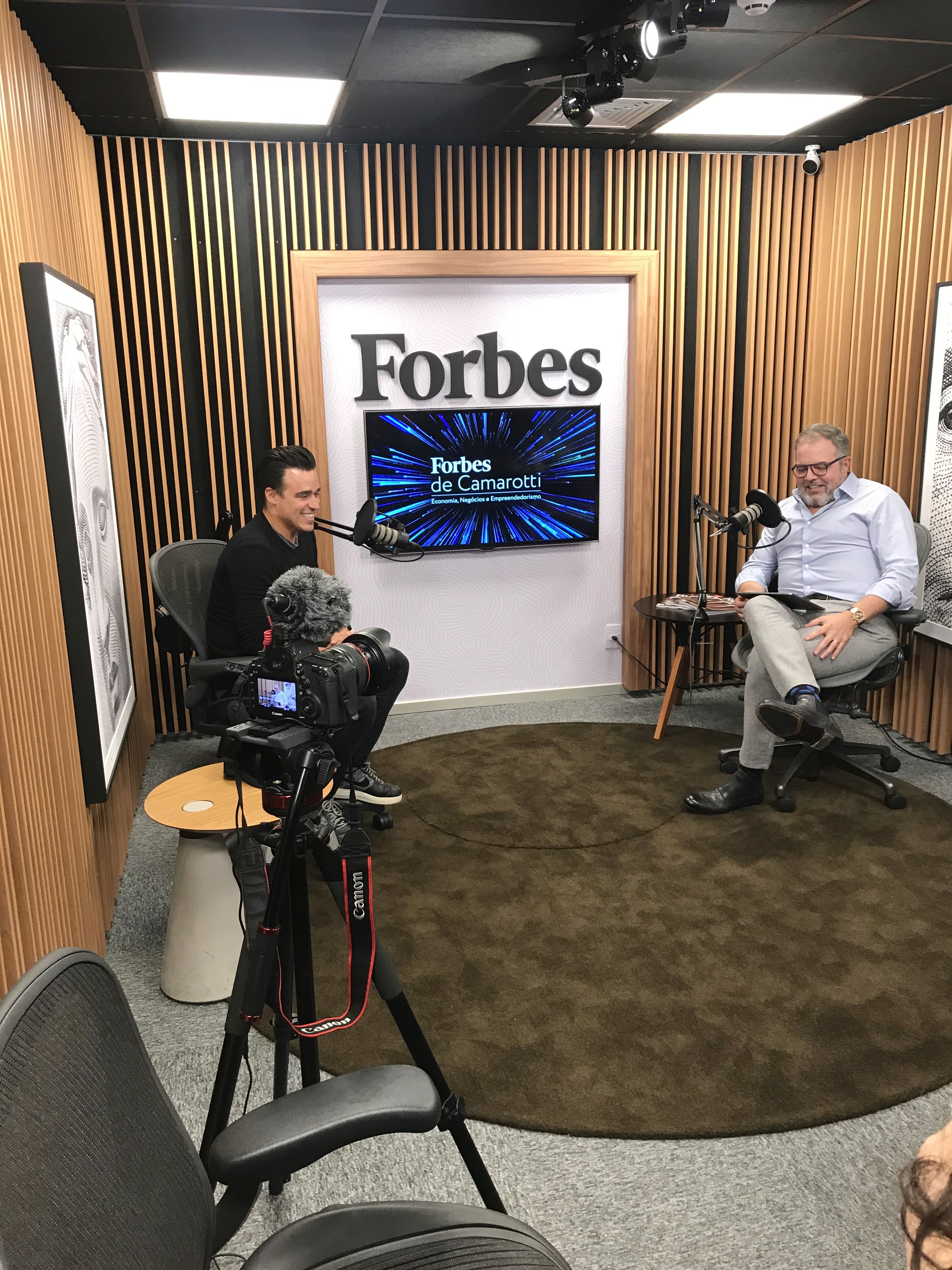 A smiling young man with crossed arms, wearing a plaid shirt and white t-shirt, poses against a dark background.