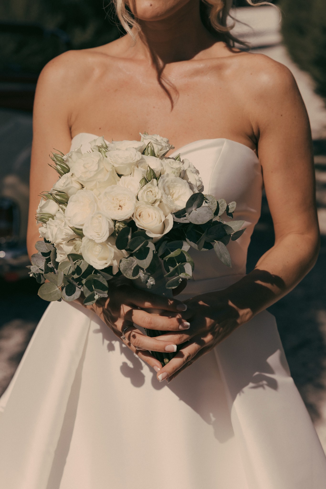 Sposa in abito bianco con bouquet di rose bianche e fogliame tra i vigneti di Bolgheri