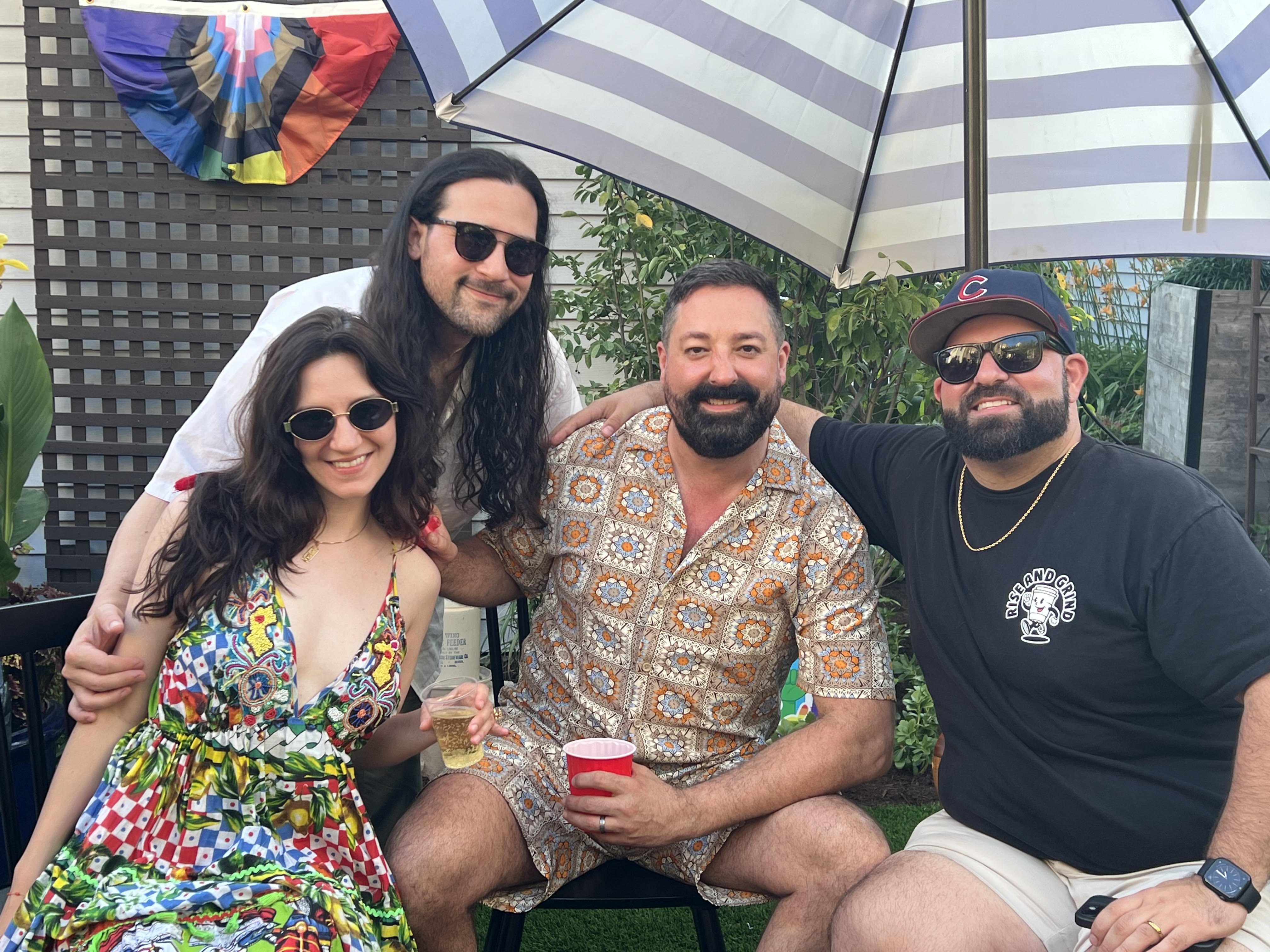 Four friends posing together outdoors, smiling, with colorful decorations in the background.
