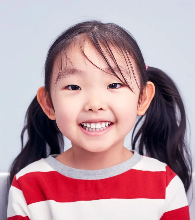 Close-up of a young Asian girl with pigtails smiling, wearing a red and white striped shirt.