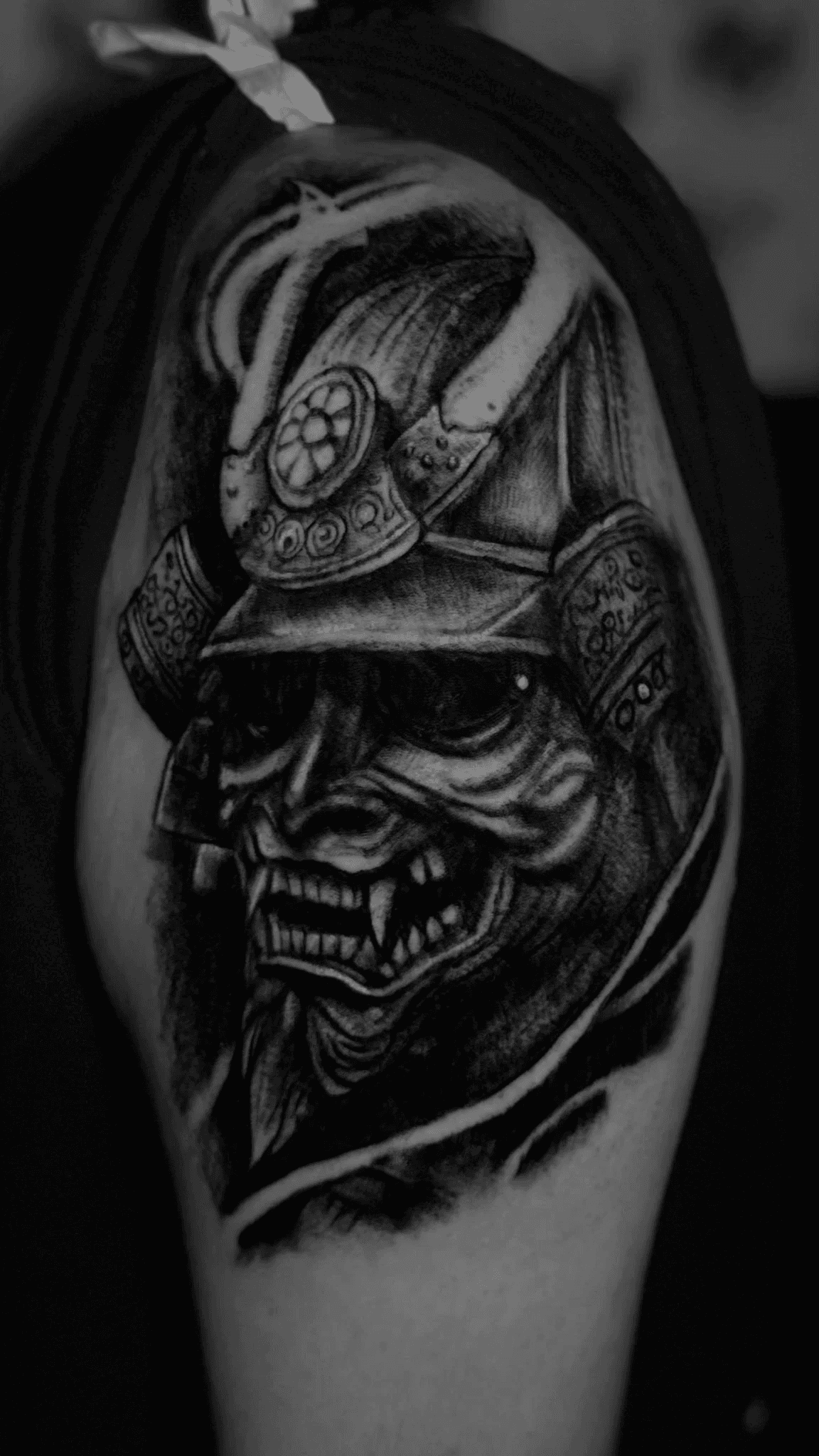 A close up of a Samurai mask tattooed on a upper arm.
