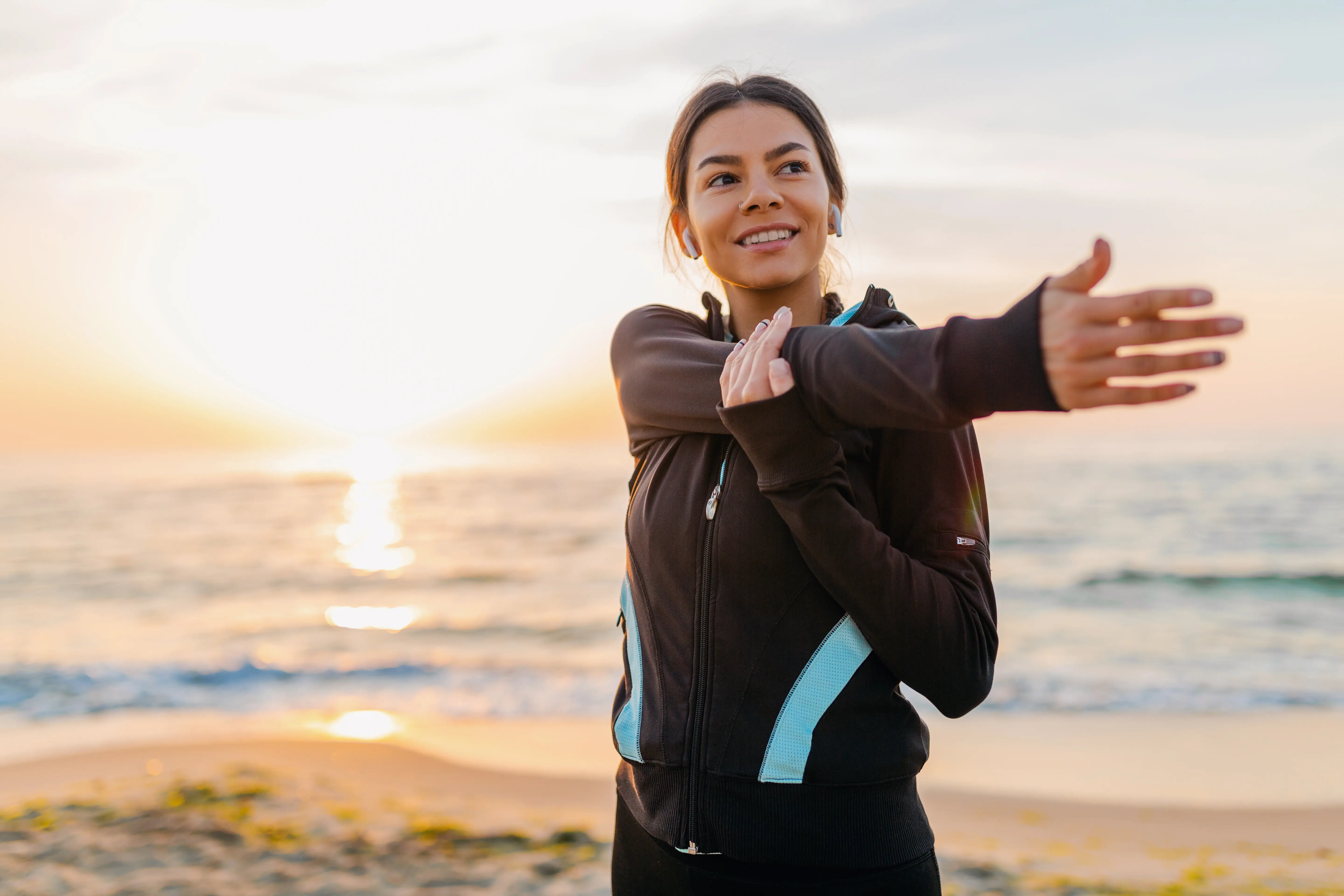 Mujer estirando los brazos frente al mar durante el amanecer.