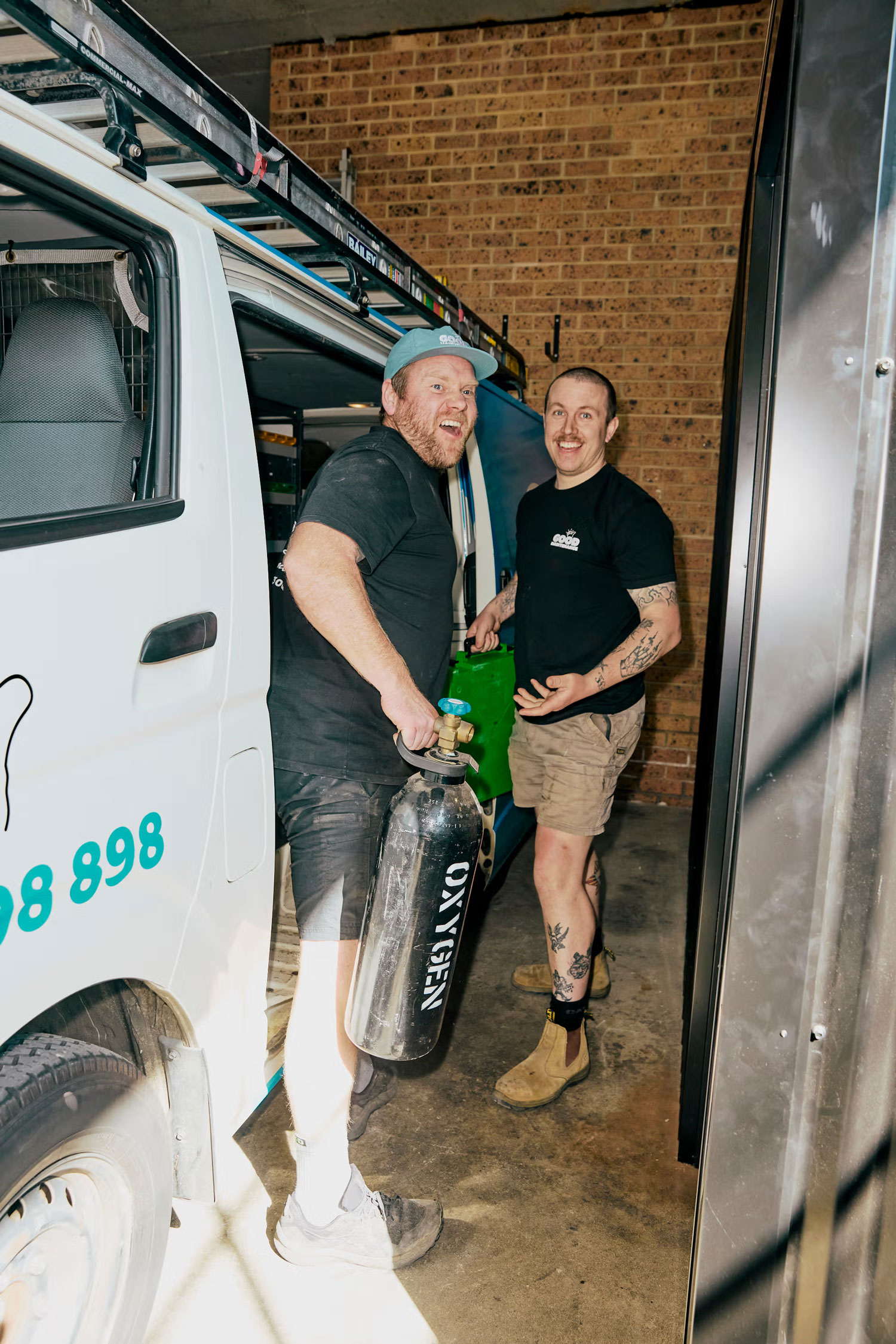 Two Team Members standing outside of an open van, smiling.
