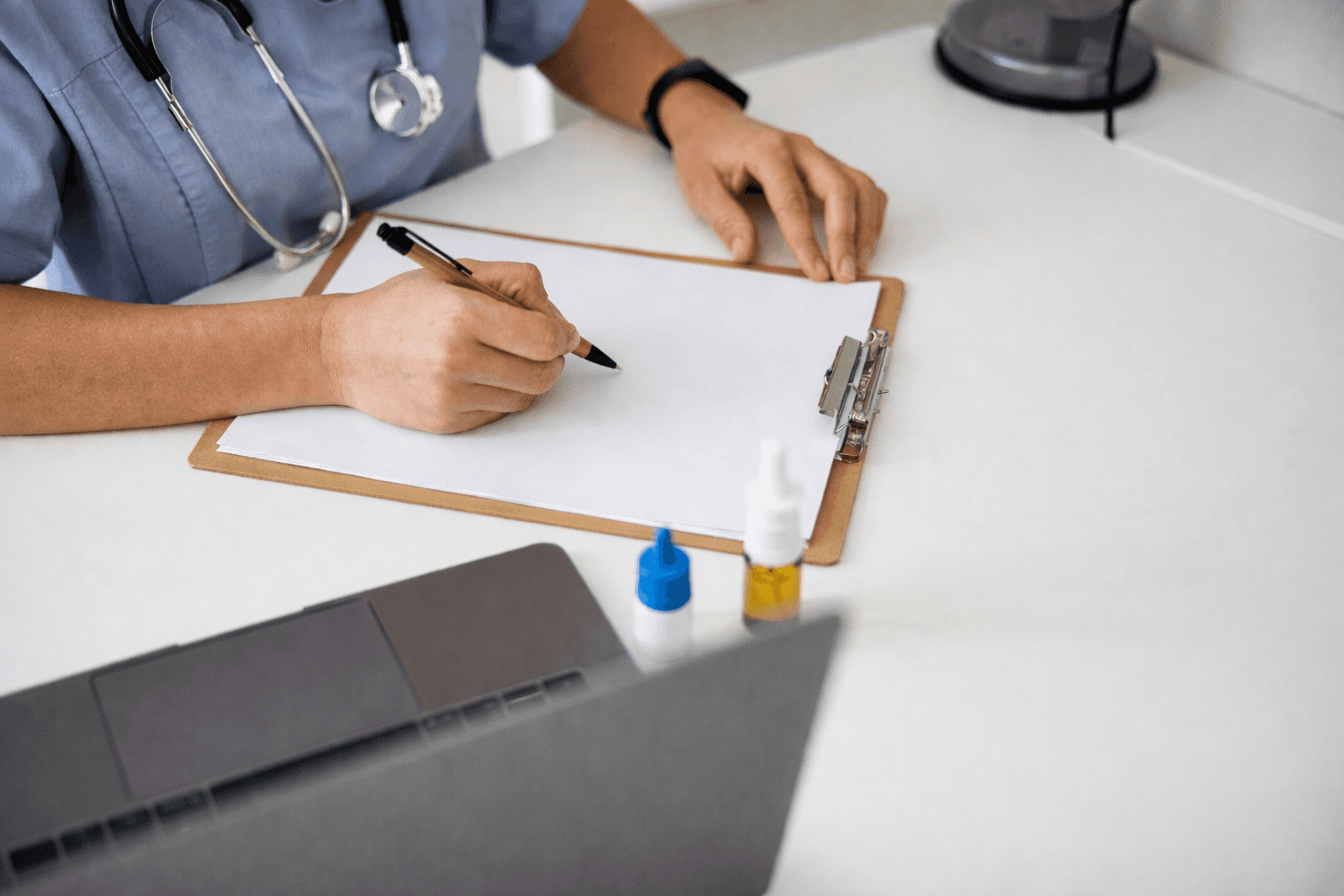Healthcare professional reviewing paperwork on a clipboard at a desk.