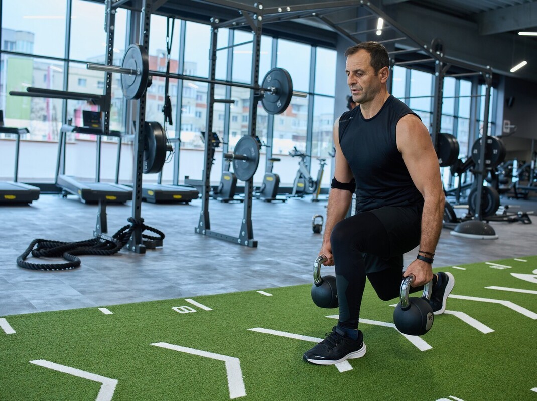older man doing lunges with kettlebells during his gym workout for weight loss