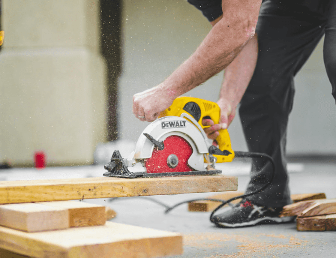 man in black sweatpants using DEWALT circular saw and cutting a wood plank