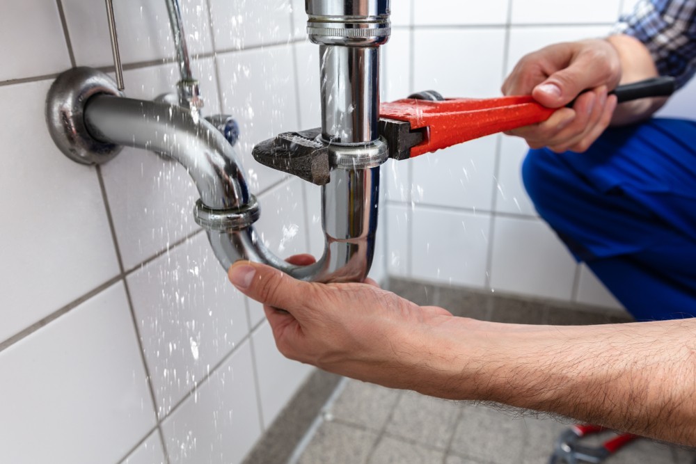 An engineer using a spanner to fix a leaky pipe