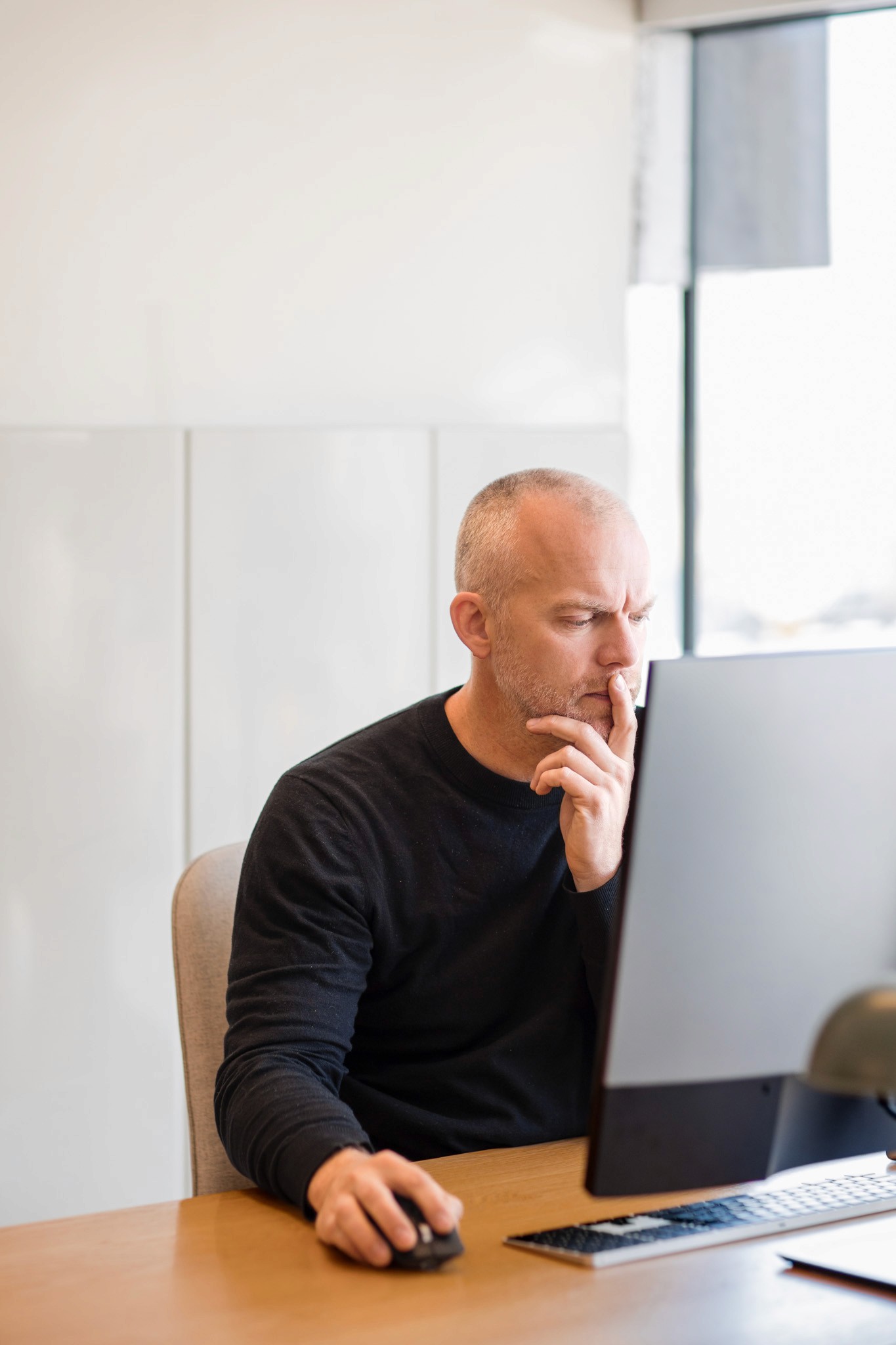 Smiling young woman with long hair standing against a dark green background, holding a finger to her chin.
