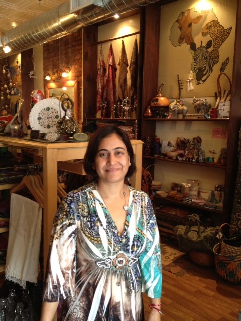 A woman surrounded by a diverse array of African and hand-made crafts in a shop, showcasing the rich cultural heritage and artisanal skills on display.