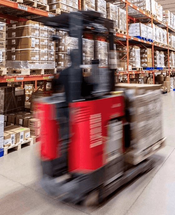 An action shot of a red forklift moving inventory through a large distribution warehouse with floor-to-ceiling storage shelving.