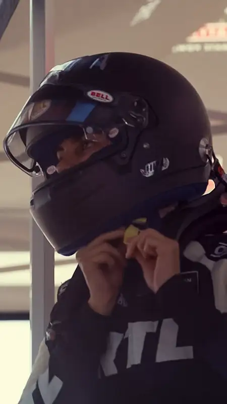Emelia Hartford, in a racing suit, adjusting her helmet before the race.