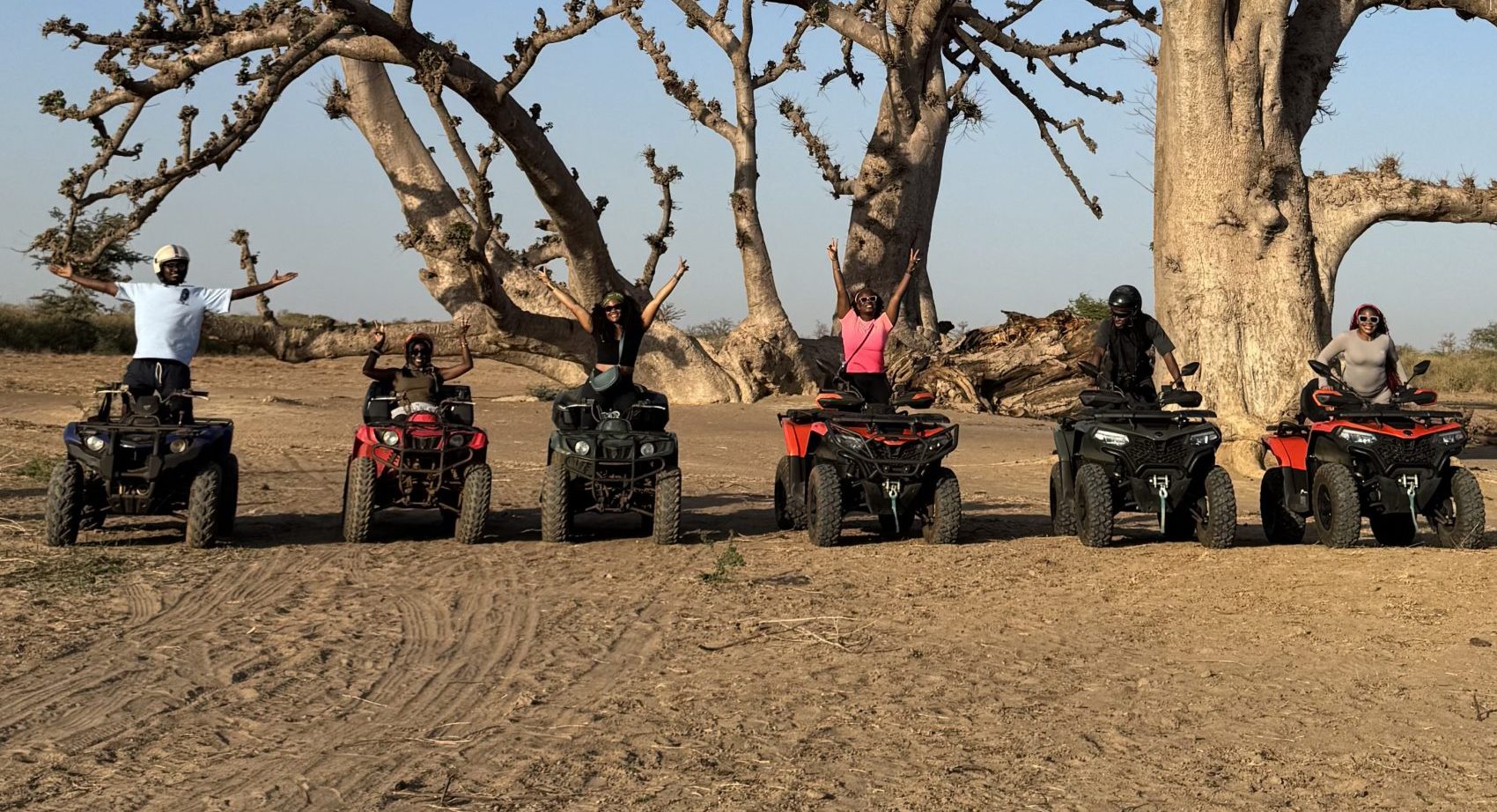 Six travellers on quad bikes with their arms raised, under baobab trees