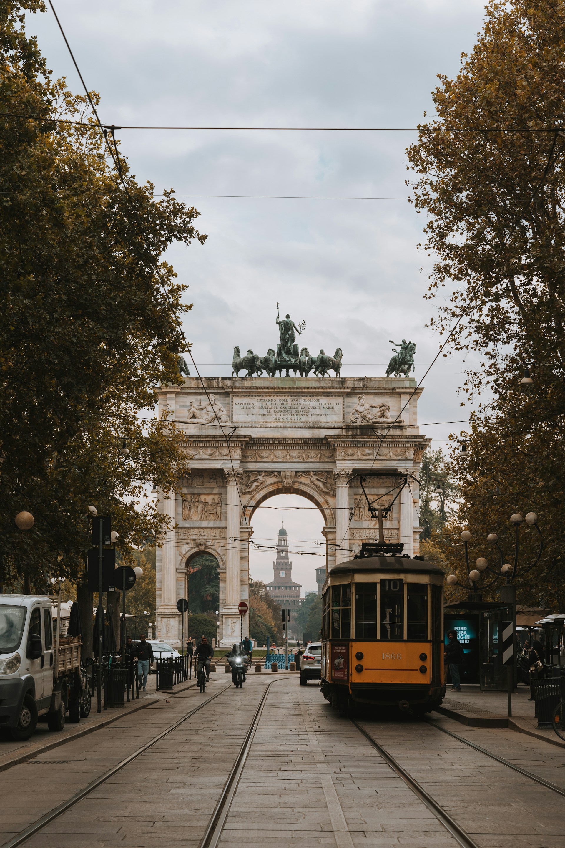 A yellow vintage tram traveling down a city street in Milan, with the Arco della Pace (Arch of Peace) visible in the background.