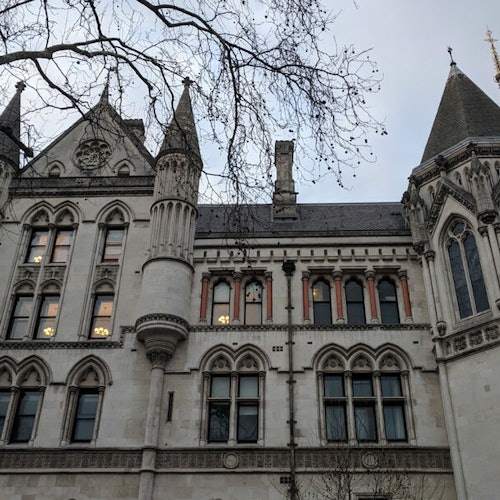 Gothic-style building facade with arched windows and tall spires, viewed from below, partially obscured by bare tree branches.