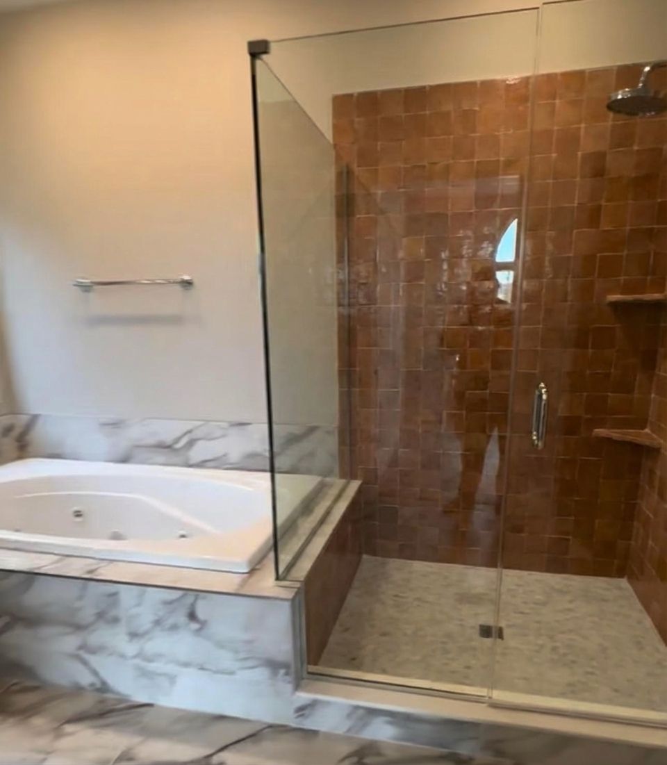 Same bathroom with warm terracotta zellige tiles on shower walls, handmade clay texture against marble