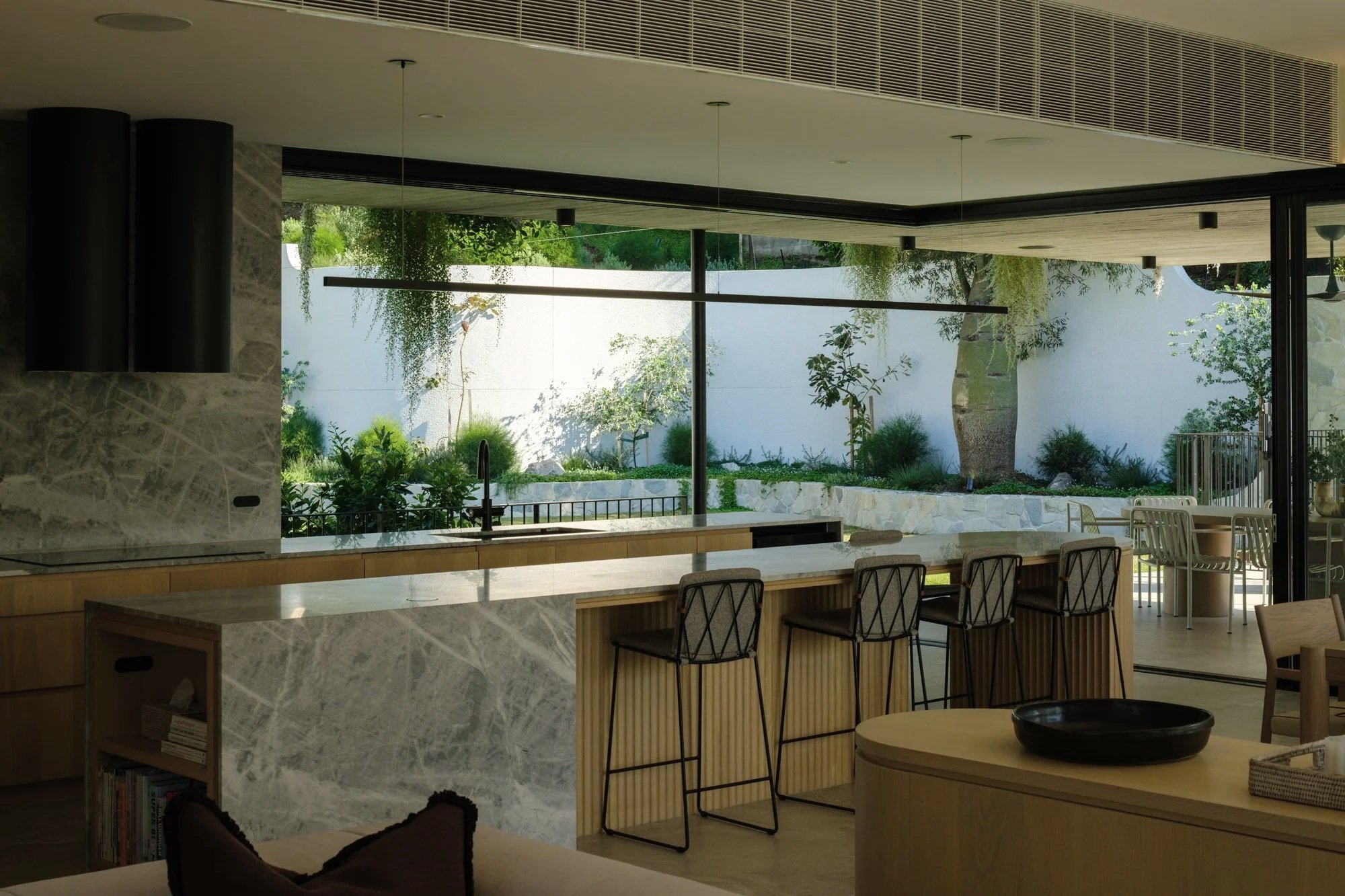 Open kitchen with marble island, ribbed timber joinery, and full-height glazing connecting to landscaped courtyard.