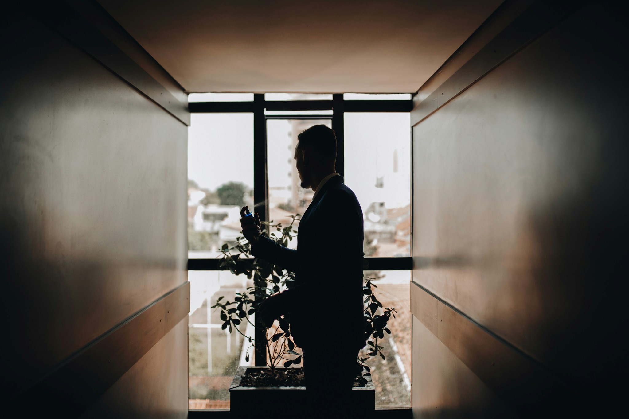 Silhouette of a groom getting ready by a window with soft backlight and a city view in the background