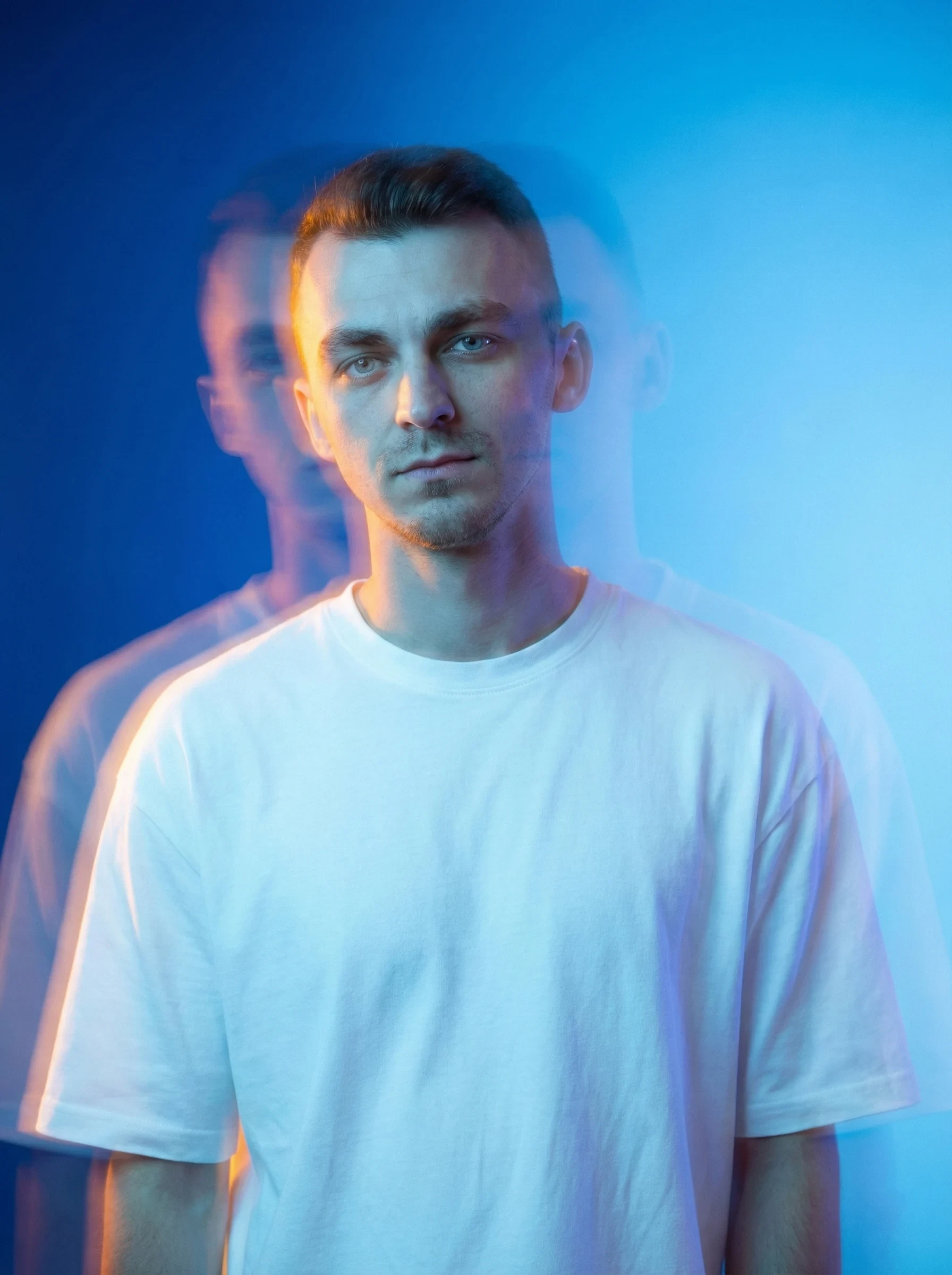 Portrait of a young man with short brown hair, wearing a white sweater, looking directly at the camera.