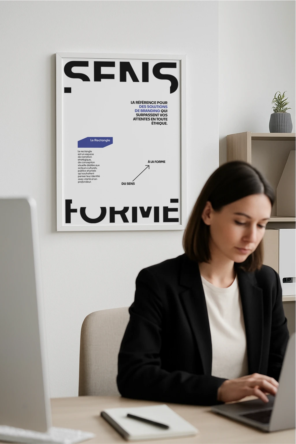 Affiche manifeste Le Rectangle version violette avec typographie sens forme exposee dans un bureau derriere une personne en veste noire.