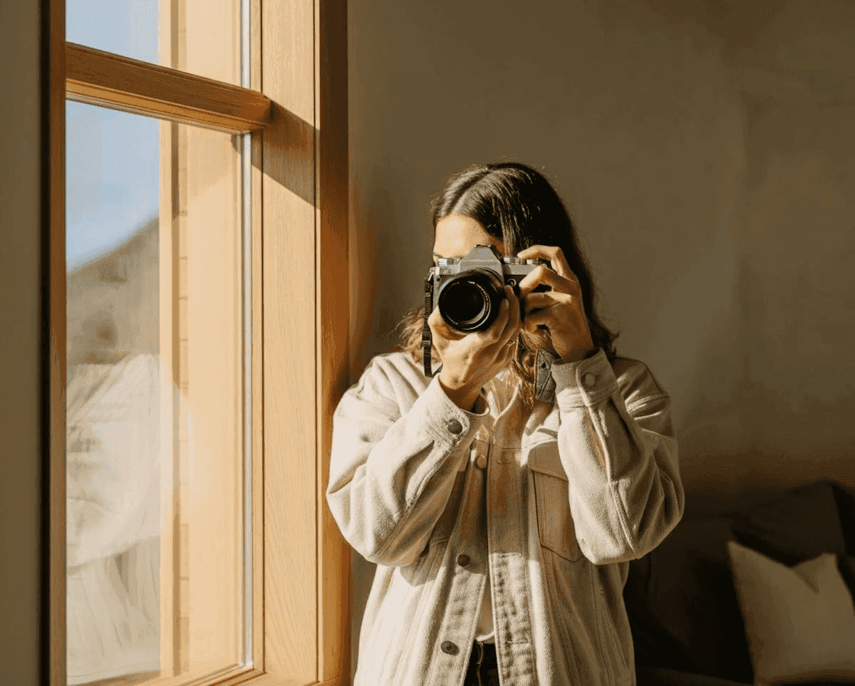 Person by a window holding a vintage camera to their eye.
