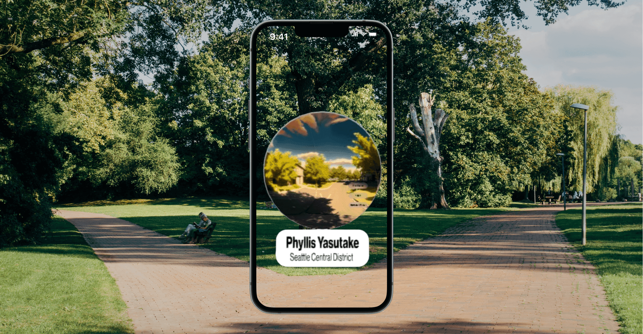 A park background with a phone in front, showing a circular portal with the text "Phyllis Yasutake" underneath