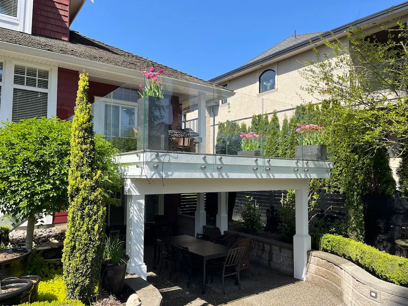 Contemporary glass railing designs featuring stainless steel standoff mounts on an elevated backyard deck.