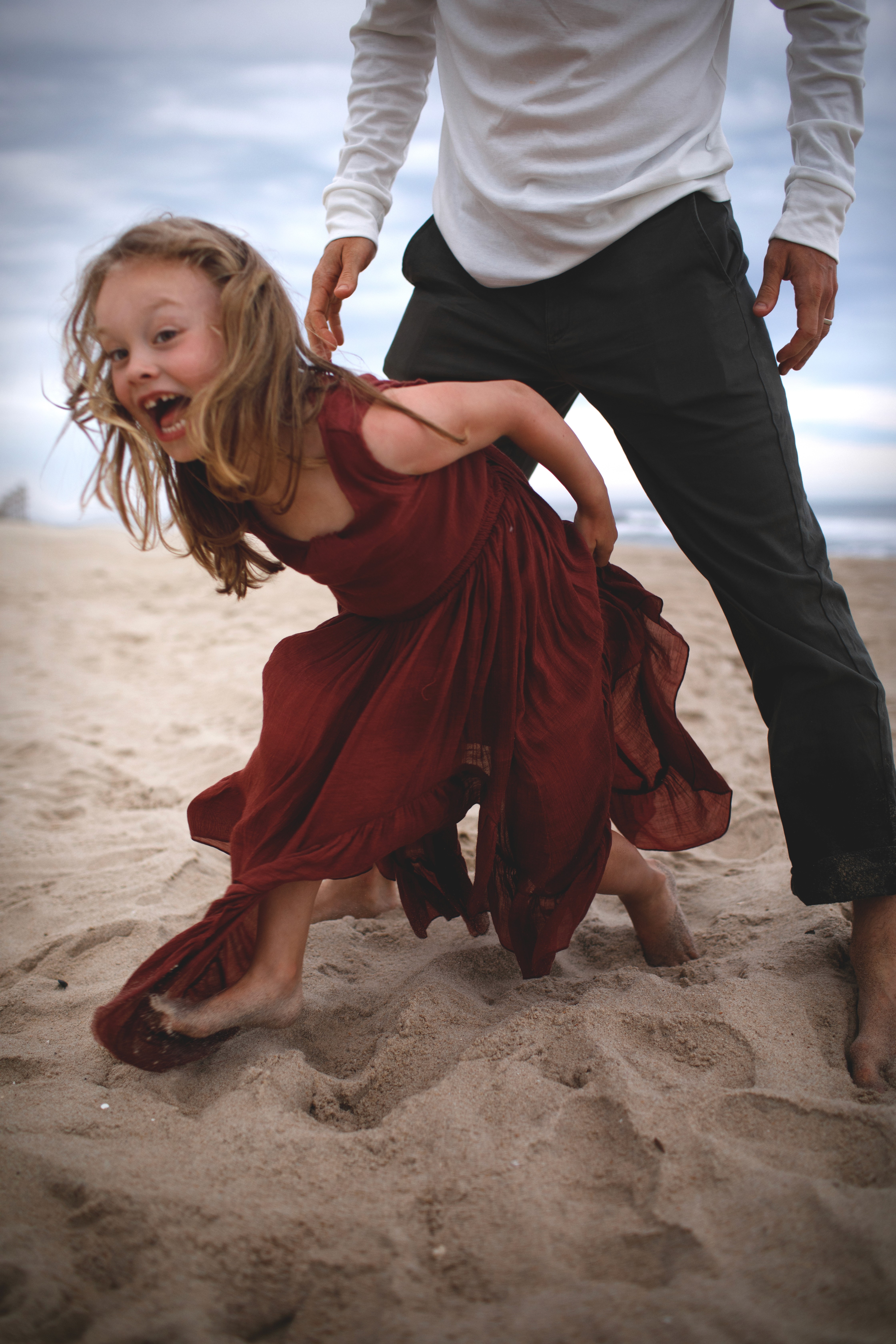 Girl running through the sand holding her dad’s hand during a family session.