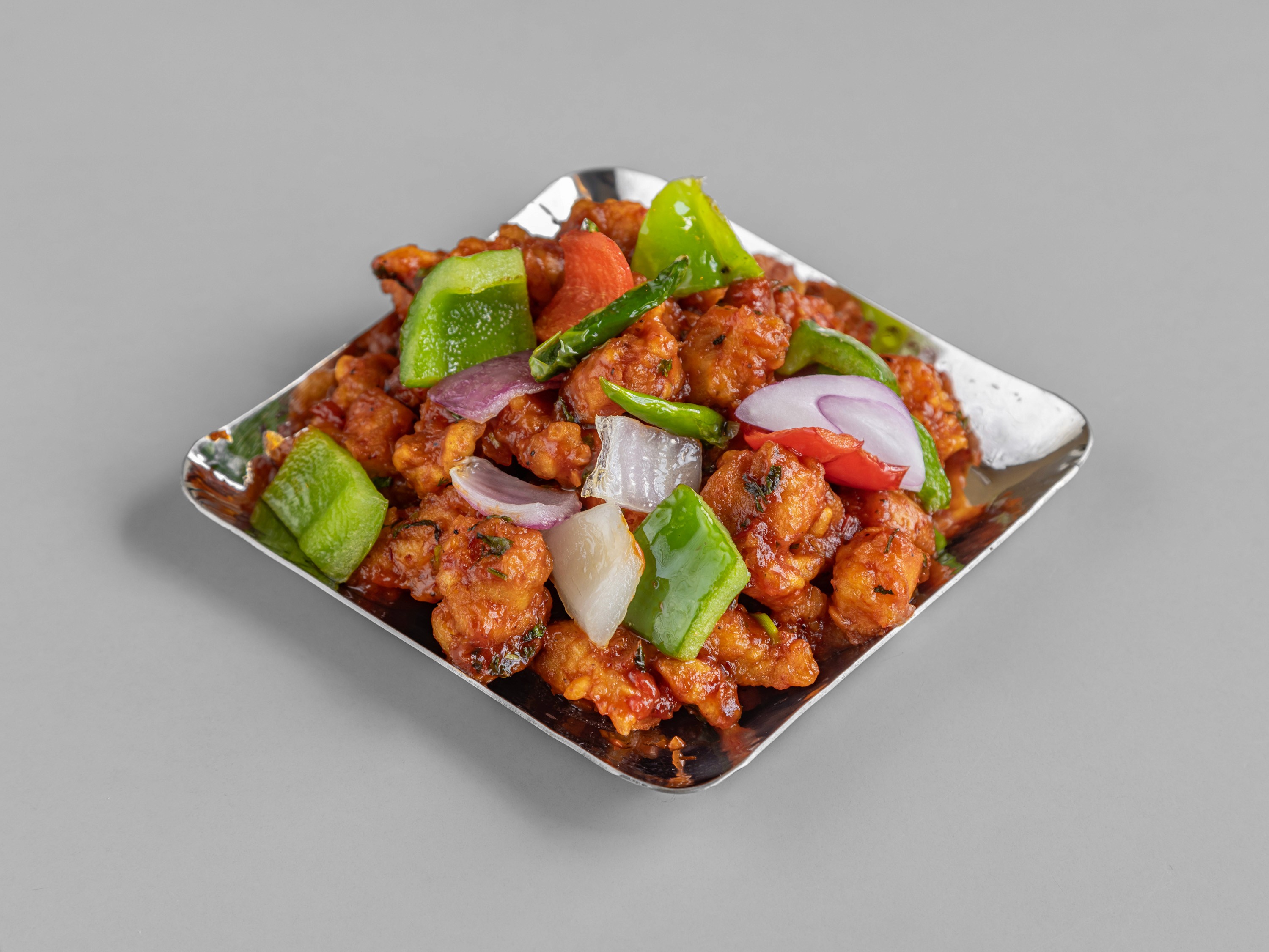 Four vibrant street-style tacos standing upright in hard shells, generously topped with shredded carrots, crispy fried protein, cilantro, and a creamy white sauce, served on a blue plate against a bright teal background.