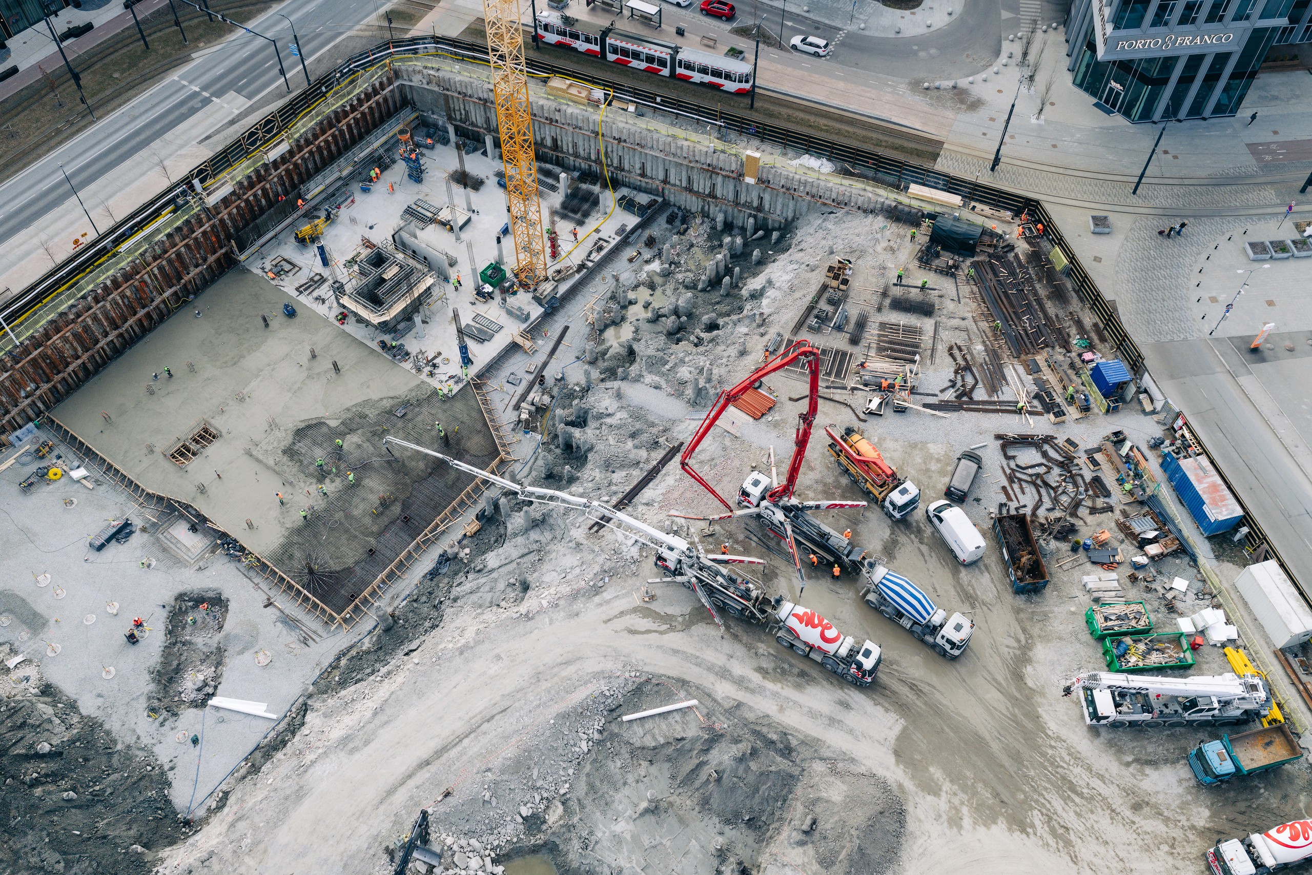 Talsinki construction progress, 14.04.2026: From above, a dark rectangular working surface, reinforcing areas, vehicles and the red pump boom divide the site into newly legible zones.