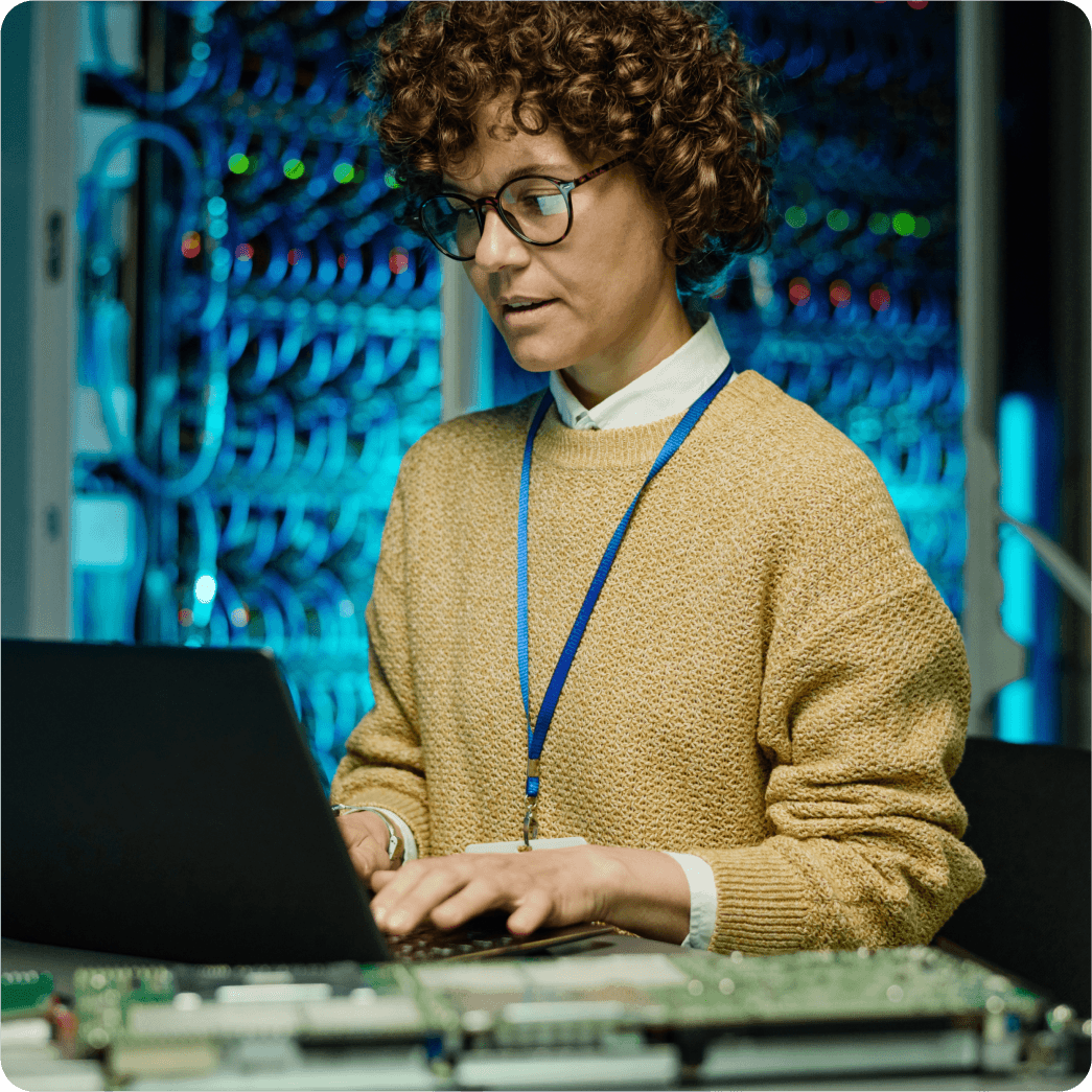 A man wearing blue shirt working on laptop inside server room