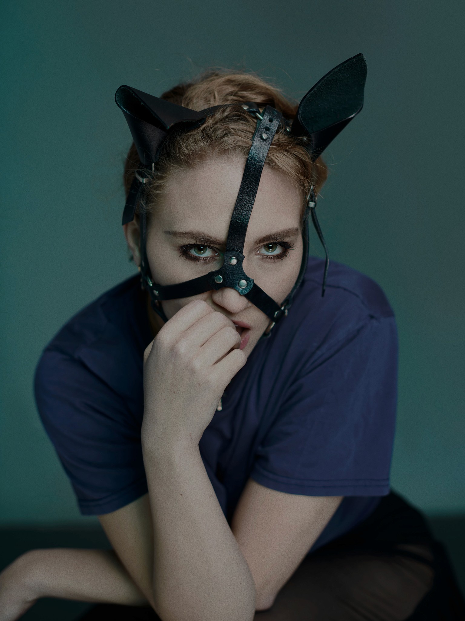 A moody studio portrait of actor, model, dancer and musician Kat Cunning. She is wearing a leather BDSM headpiece with straps and ears.