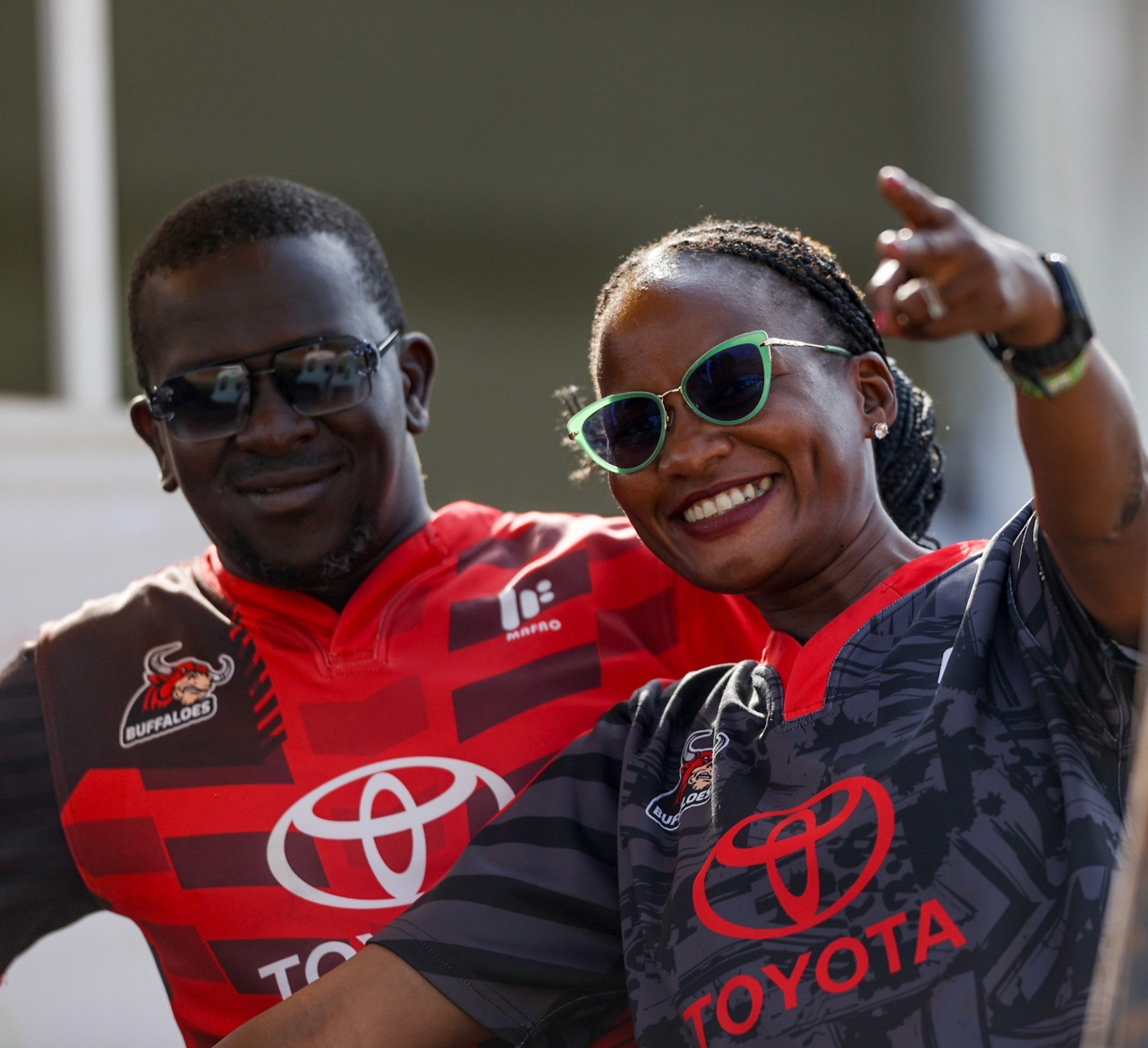 Man in blue hoodie and black shorts sitting on empty bleachers with numbered seating rows in a sunny stadium.