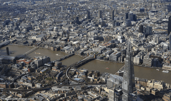 A smiling man with curly hair is sitting at a desk, looking at the camera, with a laptop and a lamp in the background.