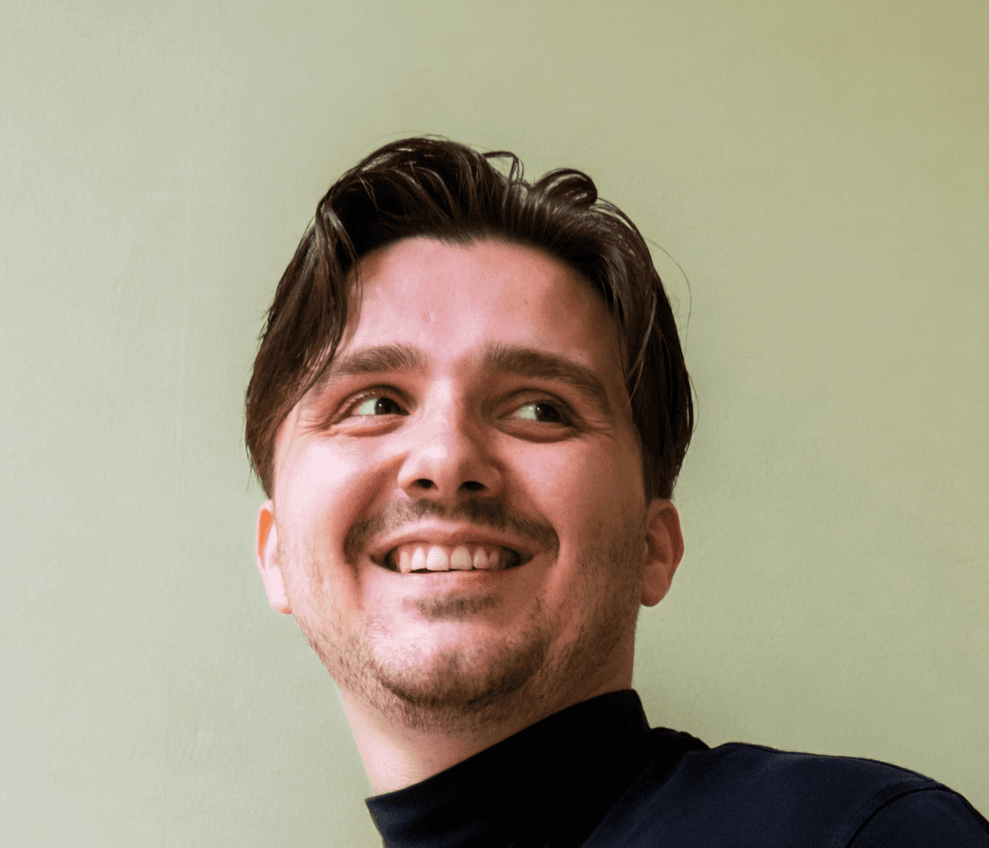 Profilfoto einer lächelnden Person in schwarzer Kleidung vor einem grünen Hintergrund