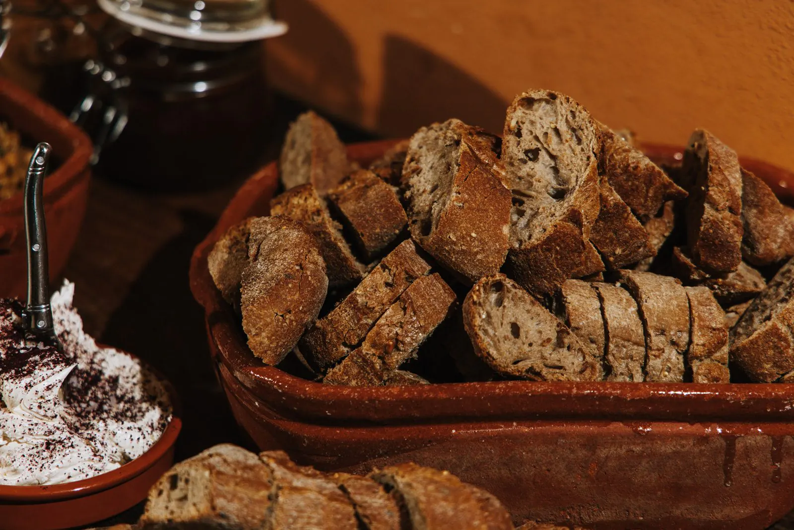 Aardewerken schaal vol sneetjes donker brood, met ernaast een kommetje witte dipsaus