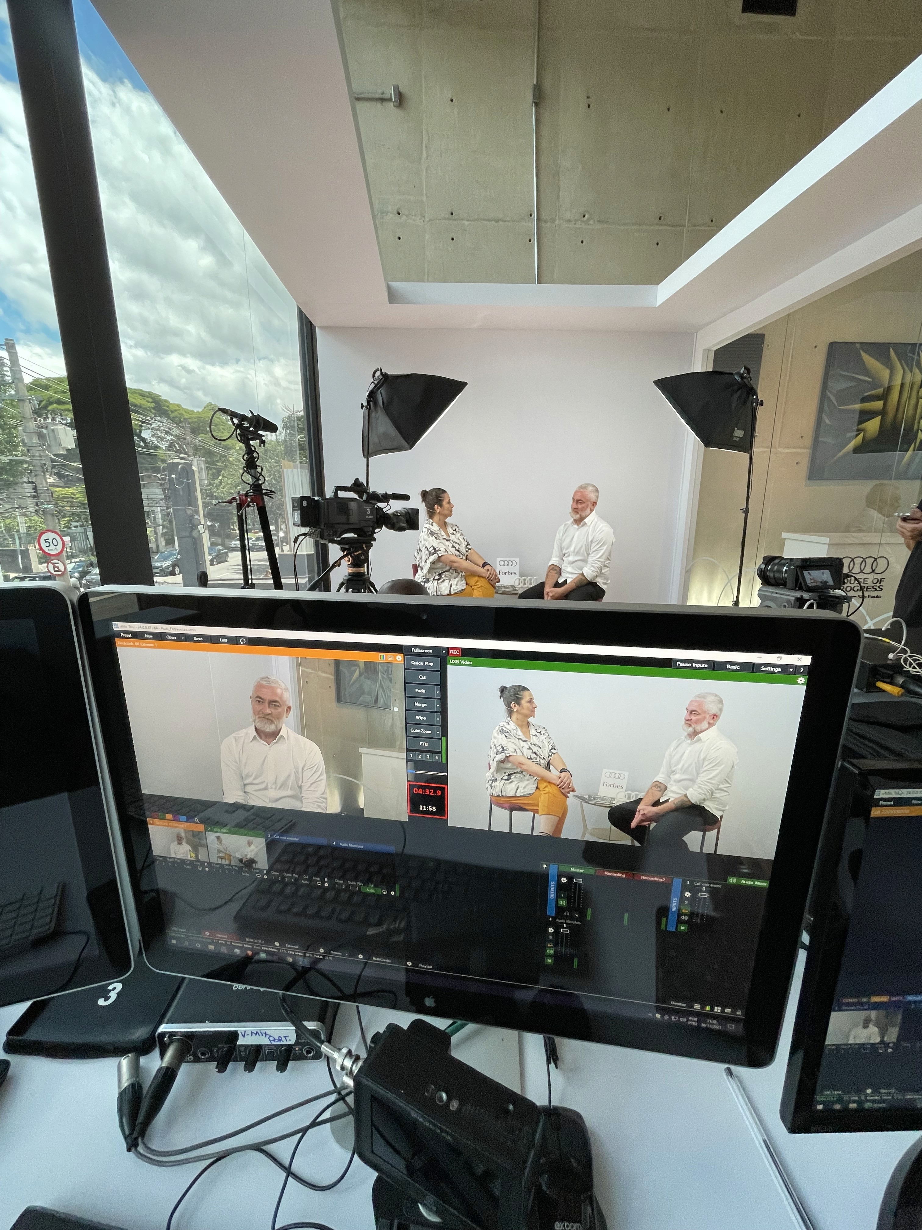 A smiling young man with crossed arms, wearing a plaid shirt and white t-shirt, poses against a dark background.