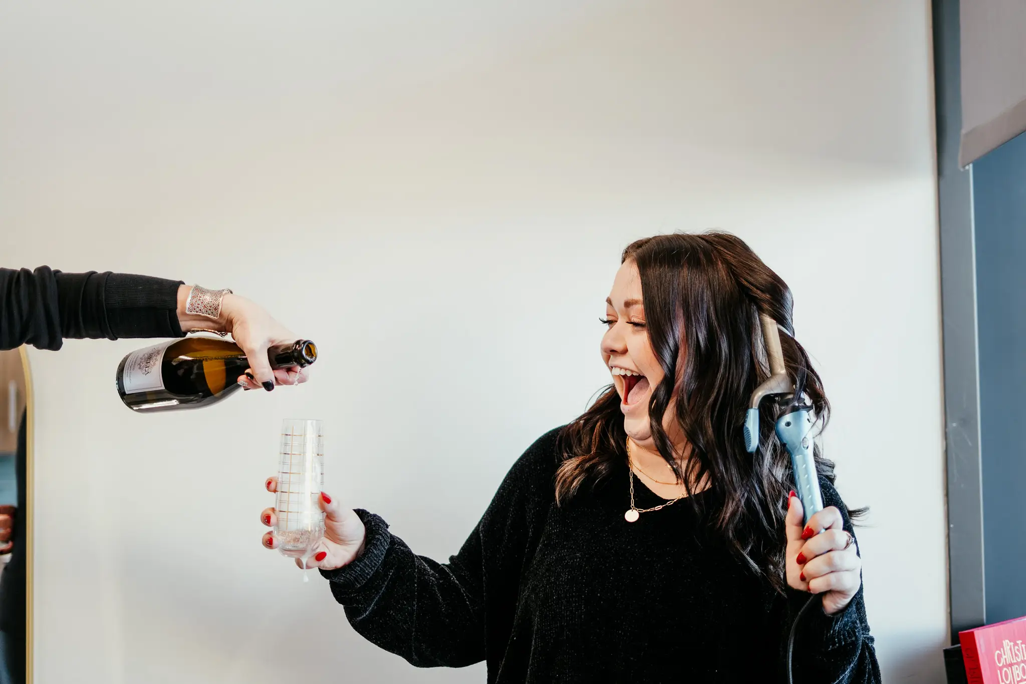 An image of a Style Me Up team member curling her hair while receiving a glass of champaign.