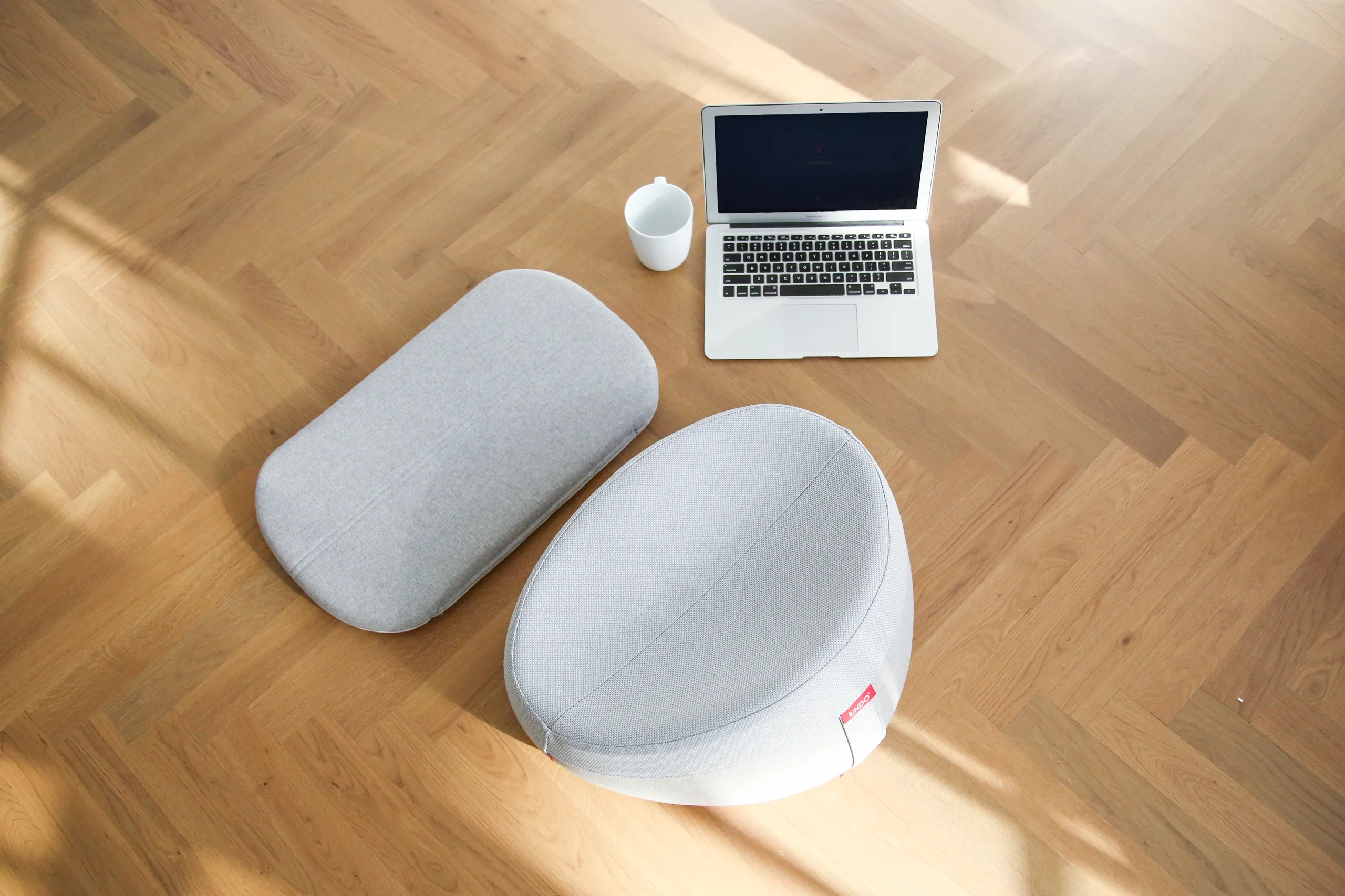 UNDO meditation cushion and removable cover beside a laptop and cup on a wood floor