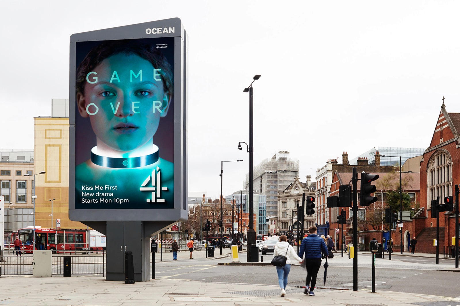 A large digital billboard in an urban street features an advertisement for a new drama titled "Kiss Me First," with a dramatic image of a person’s face and the words "Game Over," surrounded by bustling city life.