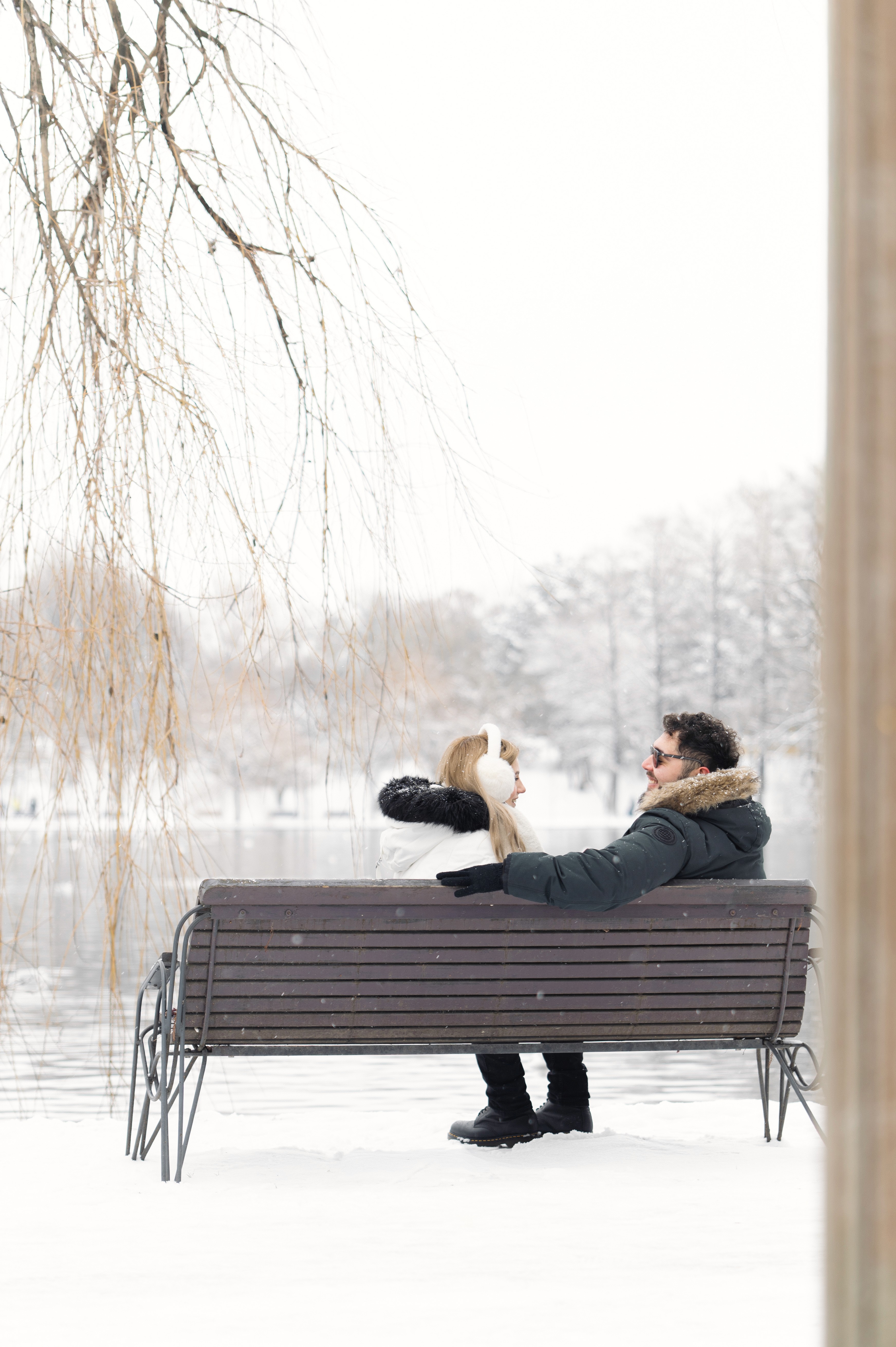 Fotografie Save the Date de iarnă cu un cuplu îmbrățișat, surprins de la distanță, într-un decor natural cu zăpadă