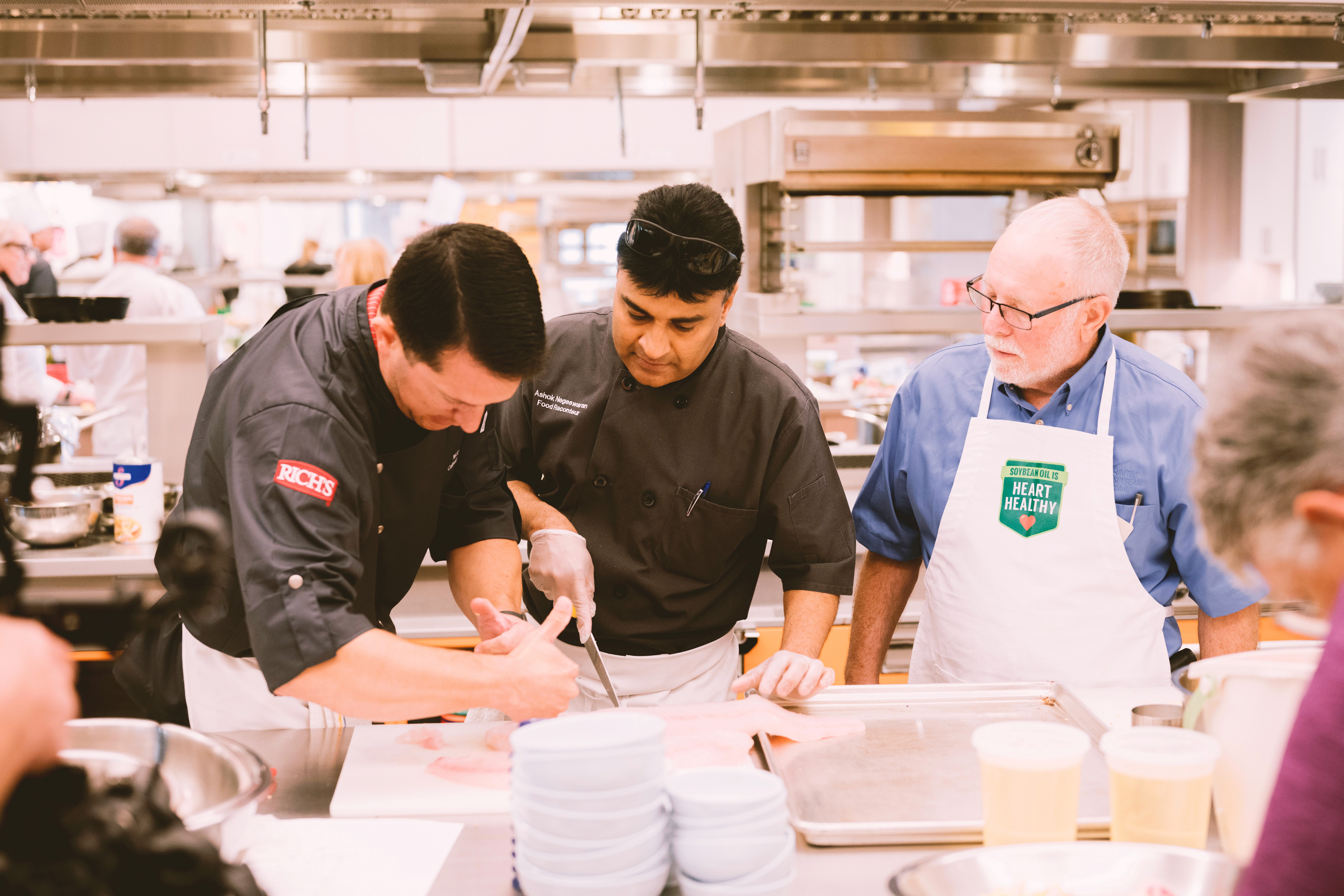 White plate with roasted carrots served on green sauce, topped with almonds and fresh herbs, held by a hand over a dark table.