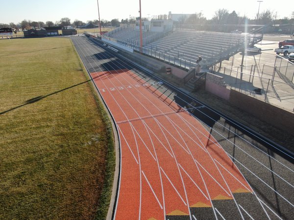 Orange and black running track curving past an empty grandstand